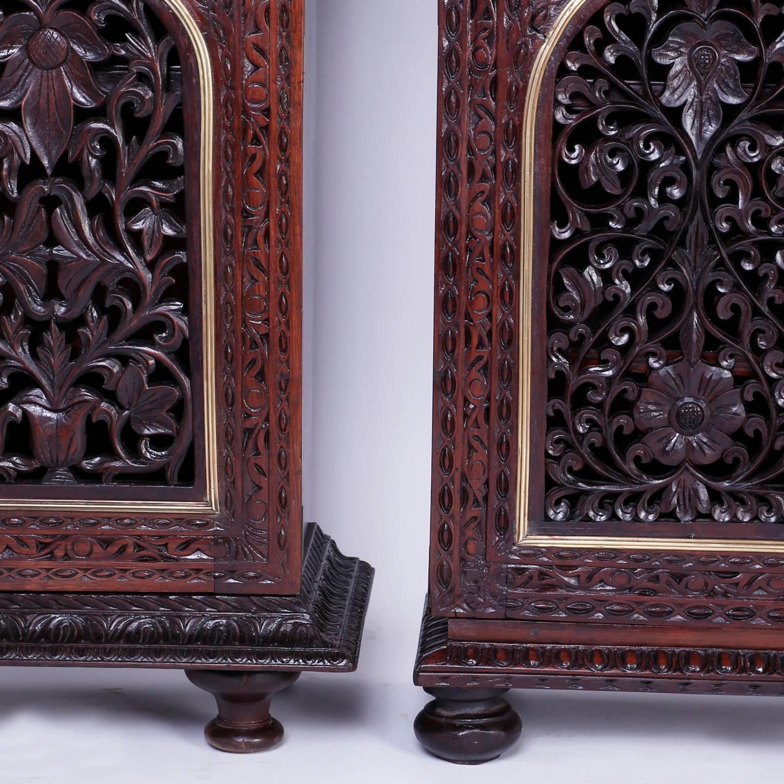 Rare antique pair of Anglo-Indian two-door cabinets with slight artistic differences. Handcrafted in rosewood and featuring expertly carved floral designs on the fronts with brass trimmed arches, both sitting on turned feet. The cabinet on the left