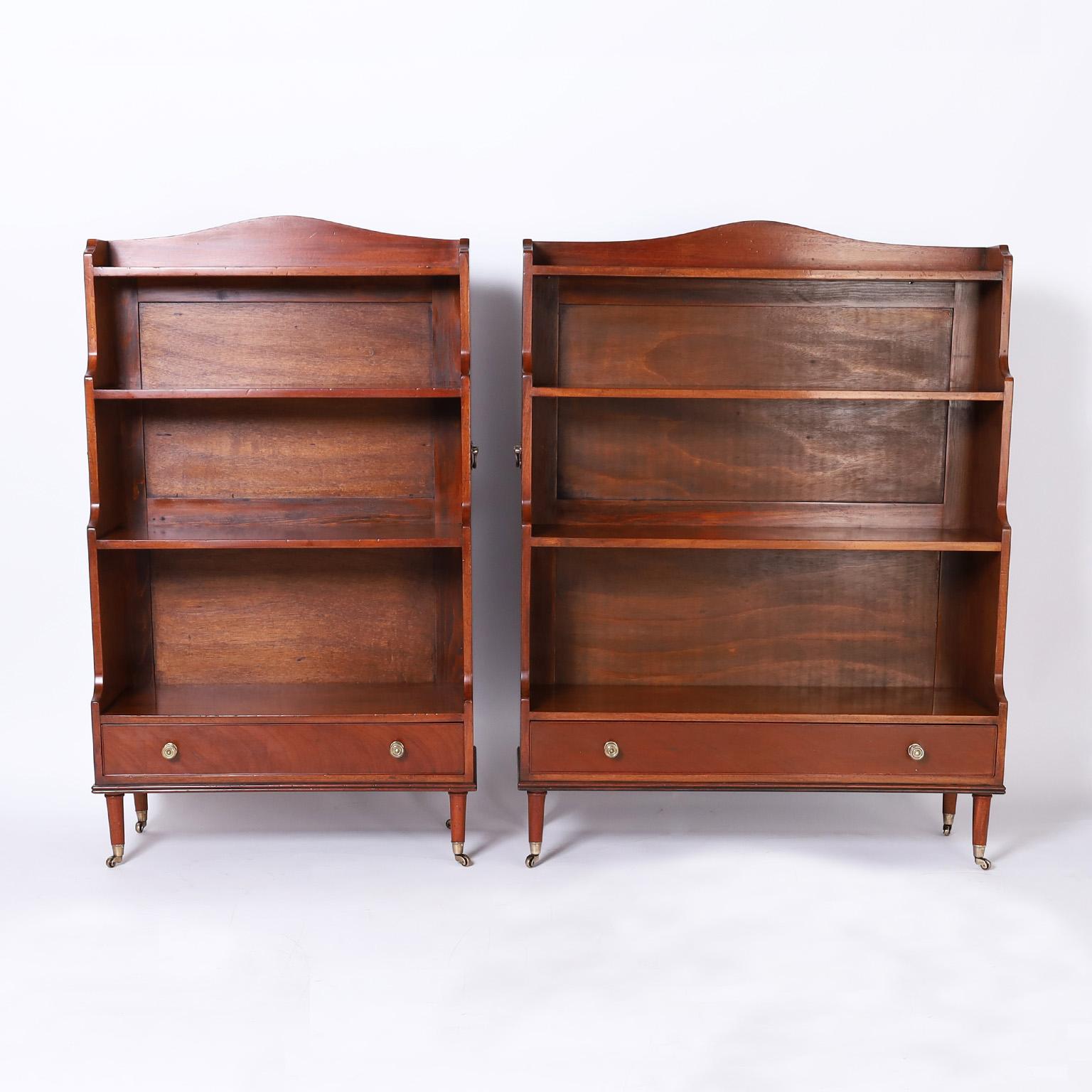 Near pair of British colonial bookcases crafted in mahogany in a step down form with brass campaign style side handles, one lower drawer and turned legs on brass casters. 

From left to right:

H: 48 W: 28 D: 13
H: 48 W: 36 D: 13.