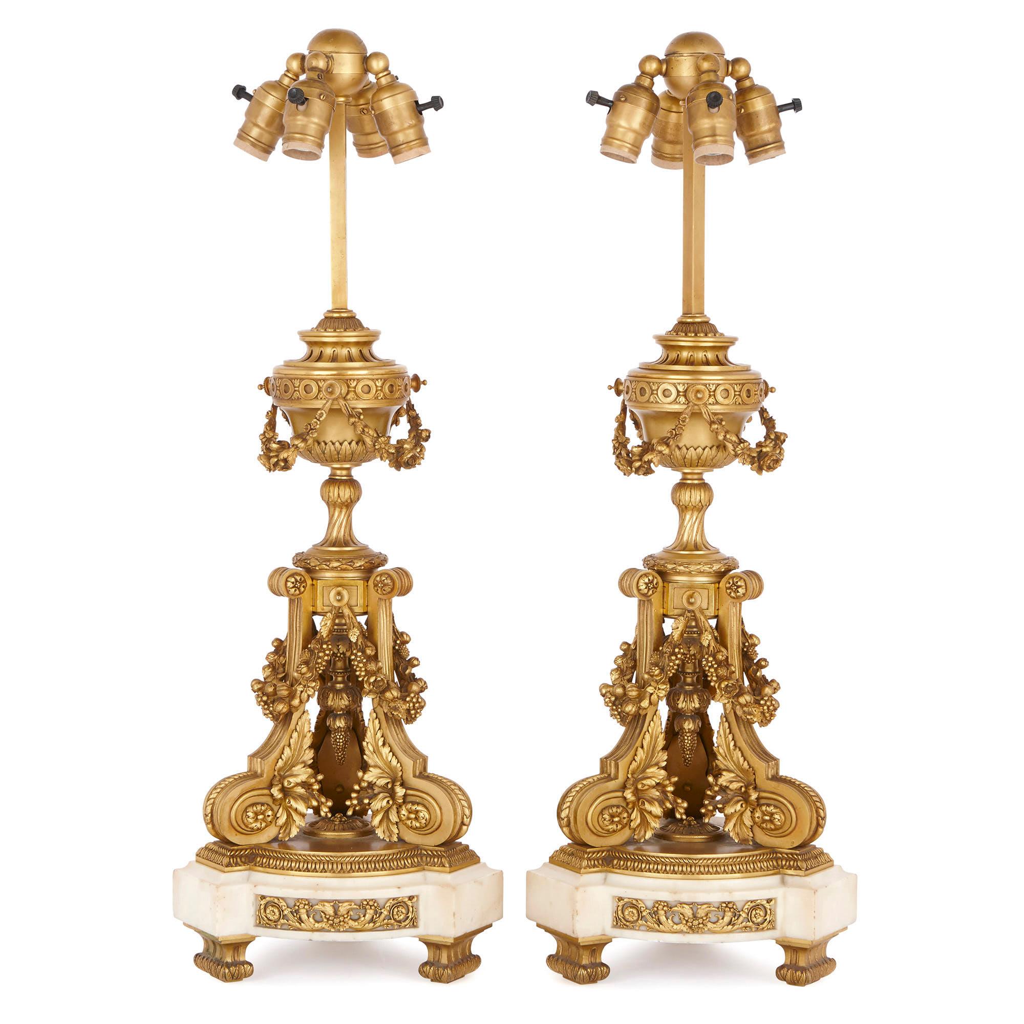 These exquisite gilt bronze (ormolu) lamps were crafted in the late 19th century in France. With their classically-inspired urns, scrolls, foliage, flower and fruit swags, these lamps are clearly inspired by Louis XV period decorative arts. 

Each