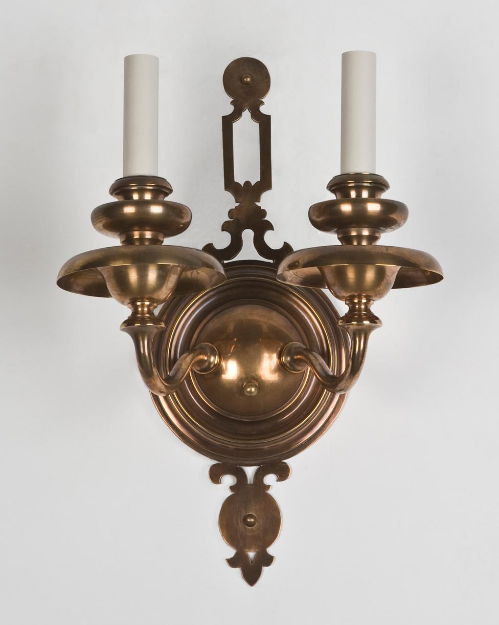 AIS2627
A pair of two arm antique sconces having circular backplates with pierced tops and broad waxpans supported by flared arms. Shown in their original coppery bronze finish. By the Meriden, Connecticut maker Bradley and