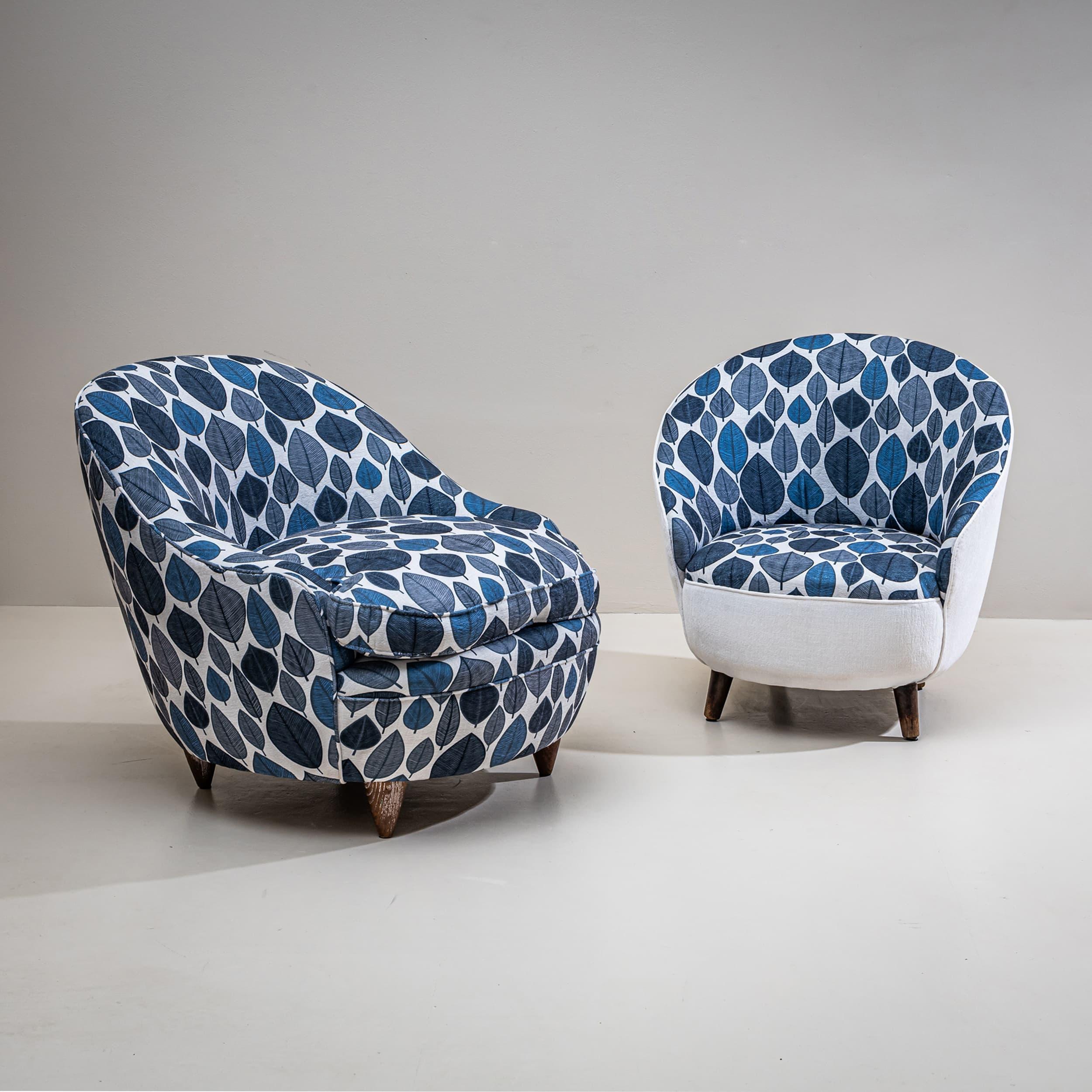 Paire de fauteuils d'exécution légèrement différente, reposant sur des pieds en bois fuselés. Les coquilles sont tapissées d'un tissu bleu à motifs de feuilles. Conçue par Gio Ponti (1891-1979) et exposée pour la première fois à la VIe Triennale de