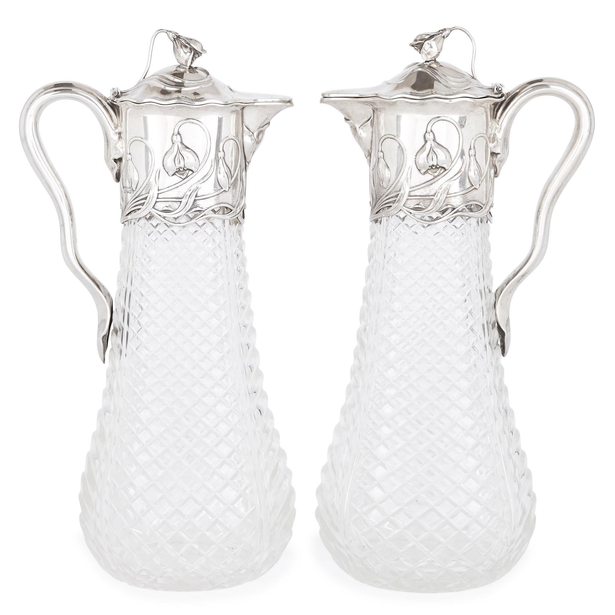 These graceful cut glass and silver claret jugs are designed in the Art Nouveau style. This style flourished in the arts in Europe in the late 19th-early 20th century. It was characterised by its use of continuous, serpentine lines and motifs, which