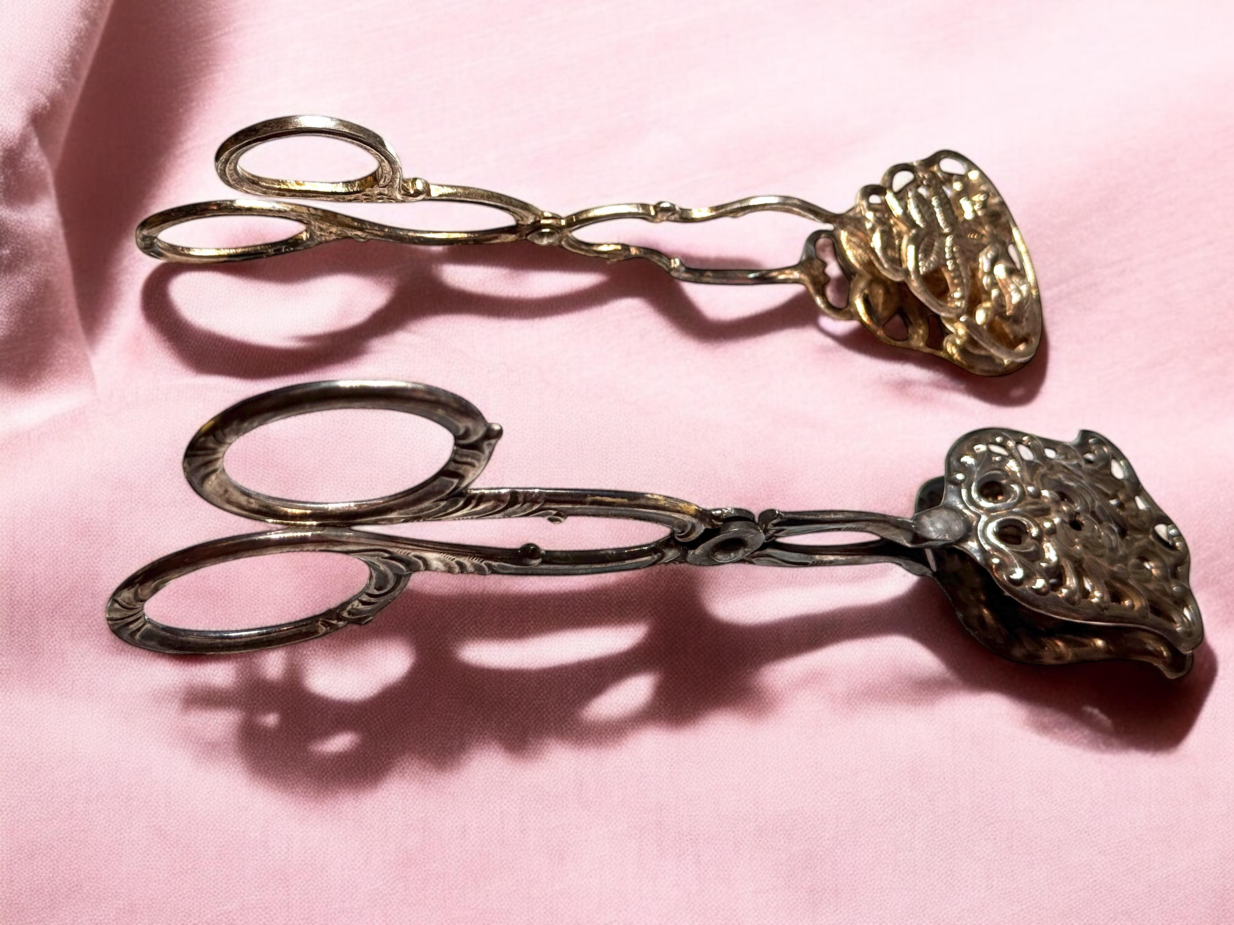 Un set di due bellissime pinze da servizio in stile Art Nouveau per pasticcini, torte, caramelle o carne. Questo pezzo da portata ha un bellissimo design. Realizzato in metallo argentato, sarà un'ottima aggiunta a qualsiasi tavolo. Le dimensioni