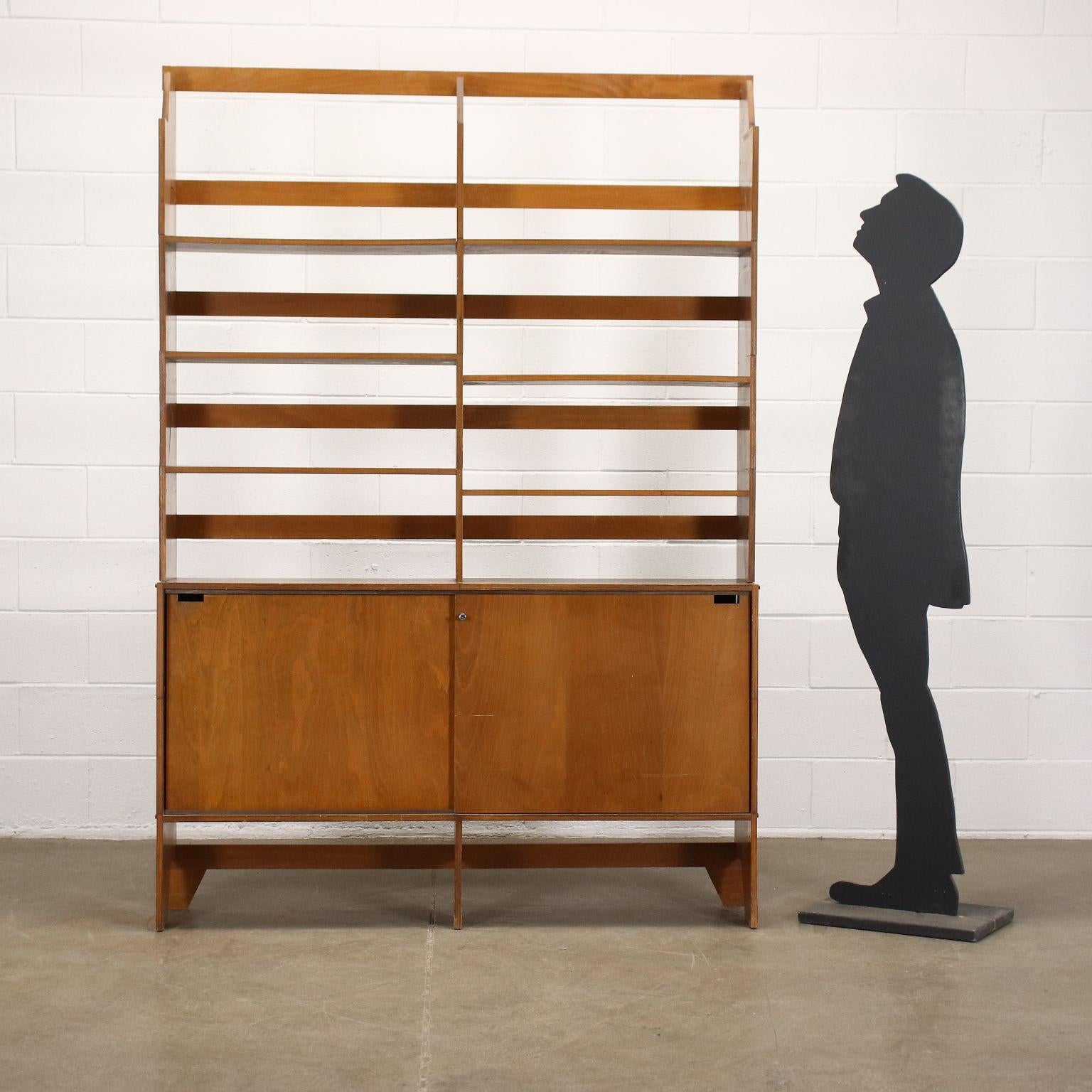 Two-bay bookcase designed in 1954. With modular and stackable elements in stained plywood, it has two storage compartments with sliding doors.