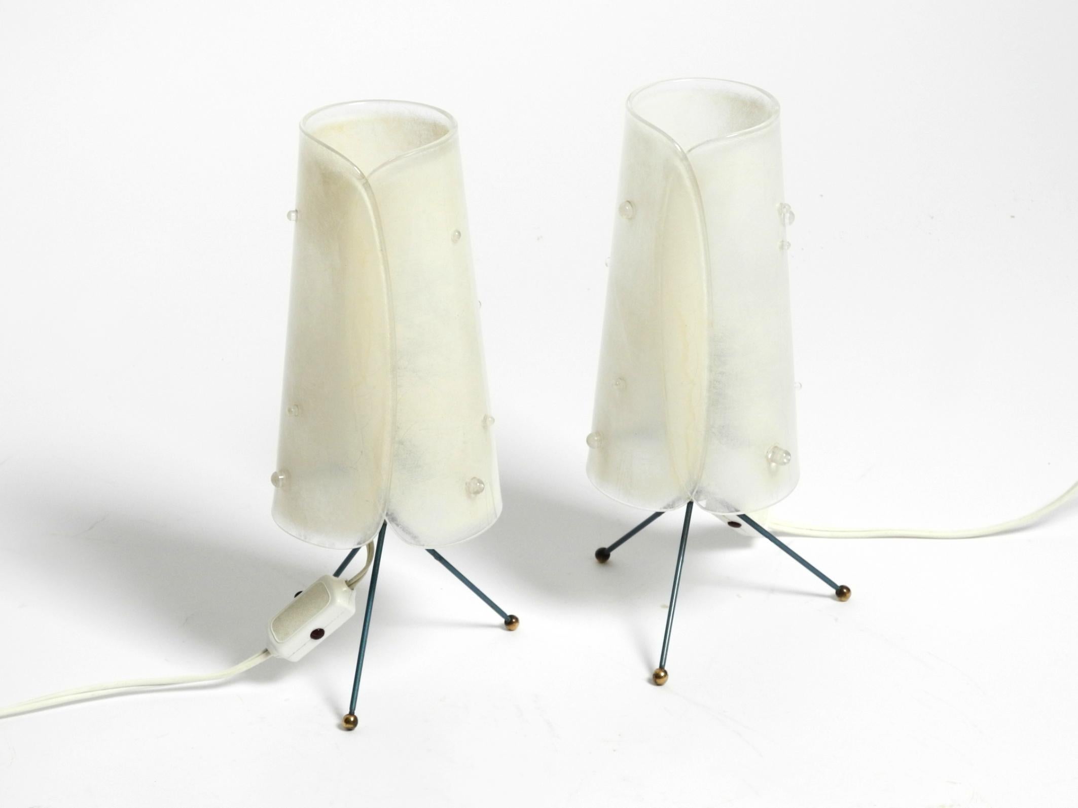 Deux belles lampes de table modernes du milieu du siècle dernier avec des abat-jours en plexiglas et des pieds tripodes en métal coloré et en laiton. Design typique des années 1950. Haute qualité.
Les deux abat-jours en plexiglas d'origine sont en