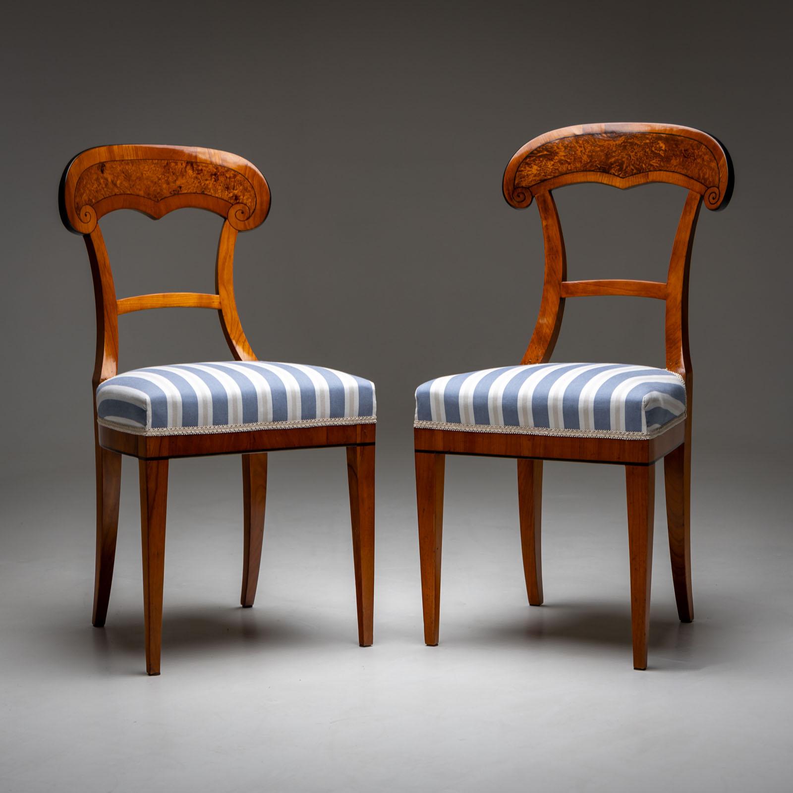 A near pair of Biedermeier shovel chairs in cherry with burl veneer and ebonized thread inlays on the backrest. The chairs stand on square tapered legs, with the rear ones slightly curved. The seats are upholstered and covered with a light blue and