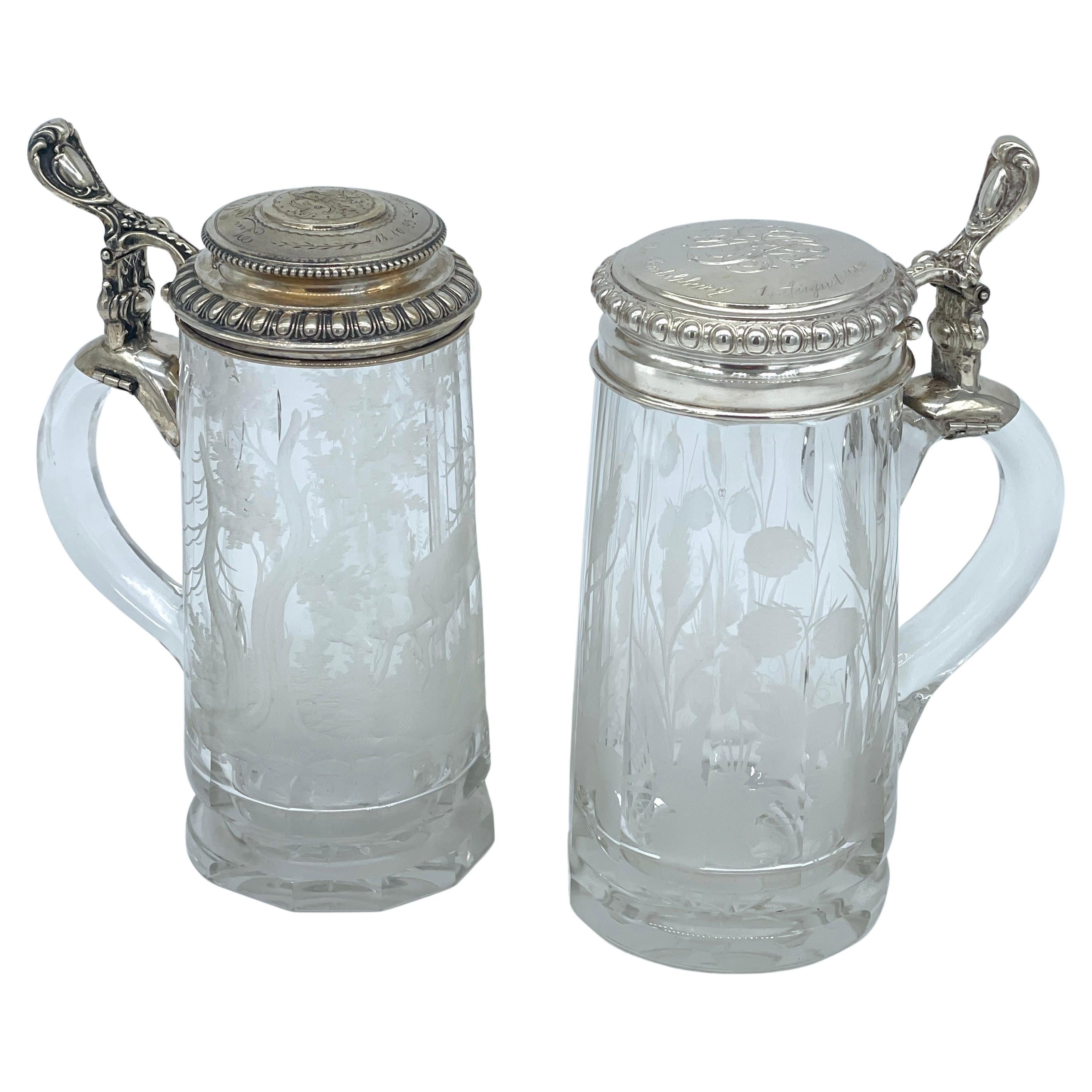 Two Bohemian Engraved Glass Steins with Stag & Clover Motifs 800 Silver Mounted Lids

Two stunning Bohemian engraved glass steins, each beautifully made from colorless crystal and embellished with finely detailed engravings. Measuring 8 inches high,