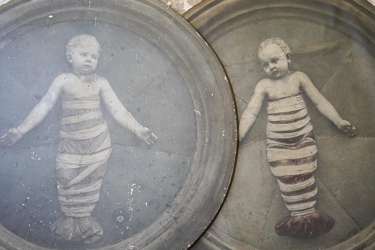 The wonderfully decorative pair of gelatin photo reliefs, each of tondo form and of good size, showing Della Robbias putto of 1487 in swaddling clothes, each sweet-faced and grasping loose swaddling bands with one hand whilst directing our attention