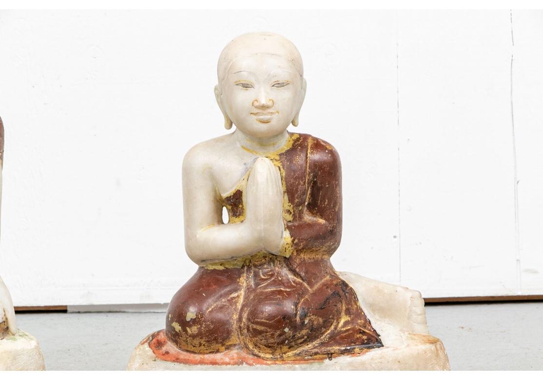Zwei kniende männliche Figuren, vielleicht Priester oder Jünger des Buddha, in weißem Marmor gemeißelt, vermutlich eine Tempelskulptur. Der eine hat die Hände zum Gebet gefaltet, der andere hat die Arme an der Seite verschränkt. Ihre Gewänder sind