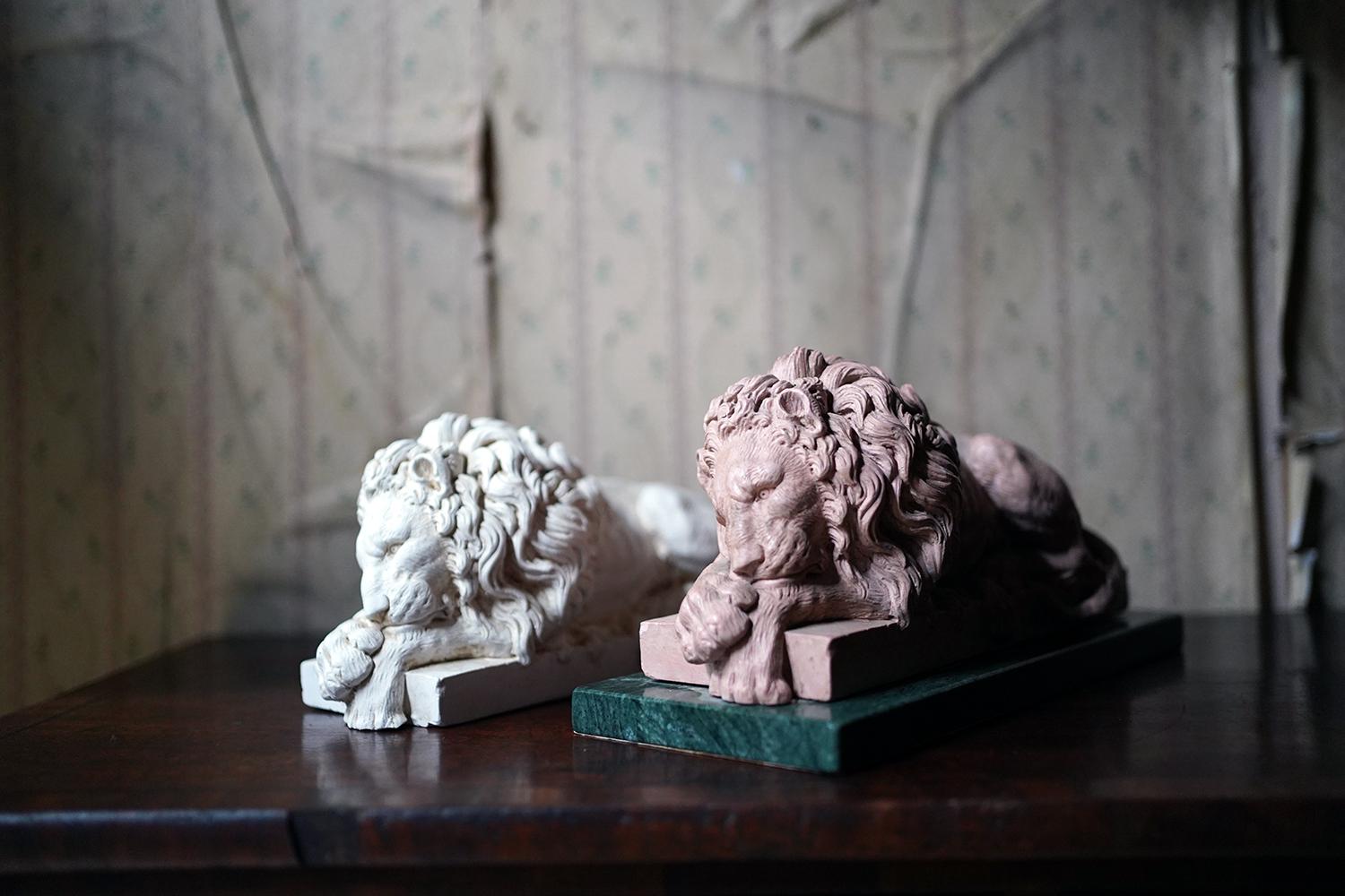 After Antonio Canova (1757 - 1822), the well-proportioned and crisply cast plaster models of recumbent lions, both sleeping, one finished in terracotta and raised on a serpentine marble plinth, the other in plain plaster, and both surviving from the