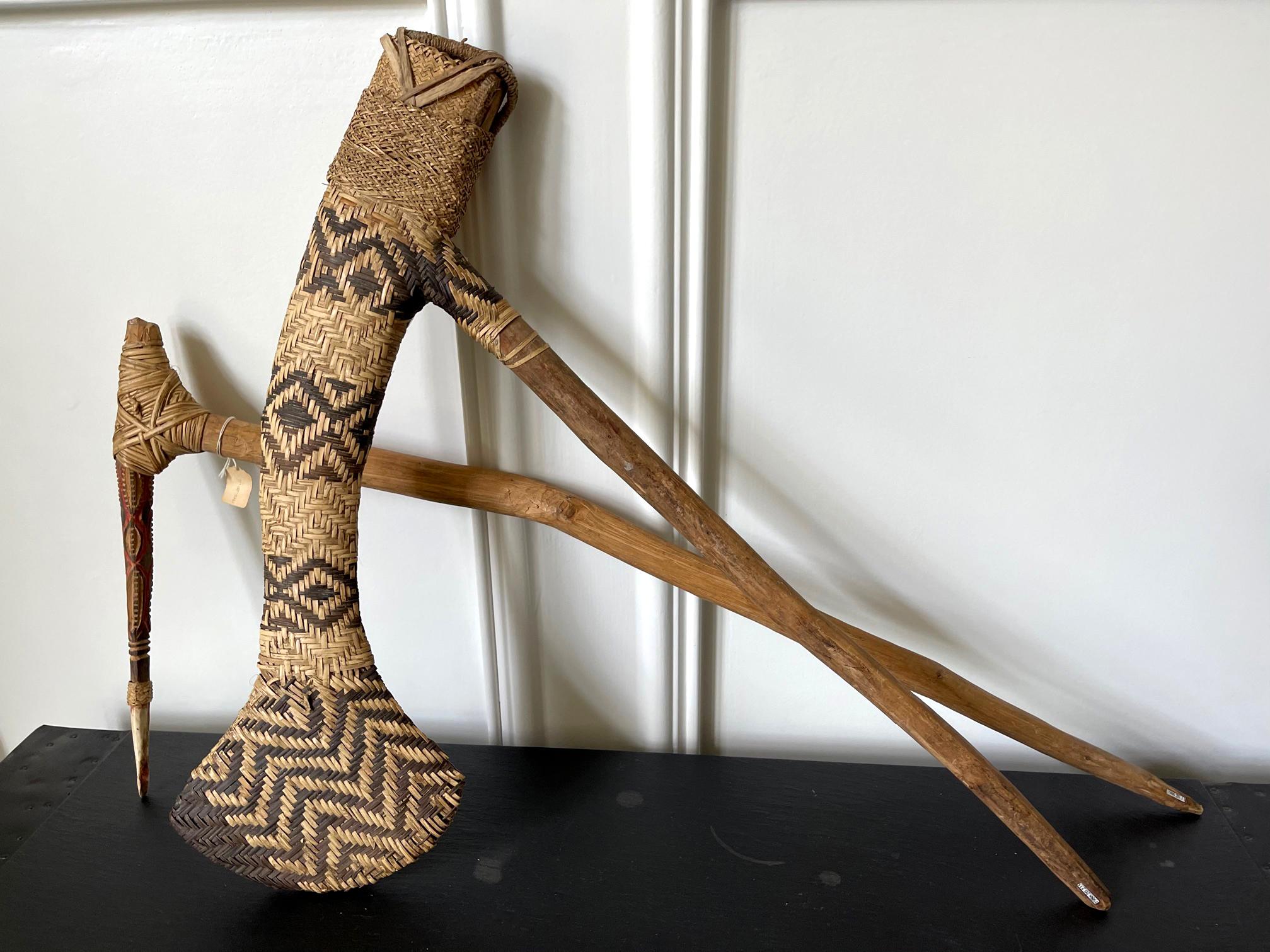Two Oceanic ceremonial weapons from PNG highlands circa 20th century. It consists of two pieces. The first is an ax with a wood shaft and a flat elongated head wrapped in finely woven rattan sheath with geometrical patterns Size: 25 1/2''L, 20''W.