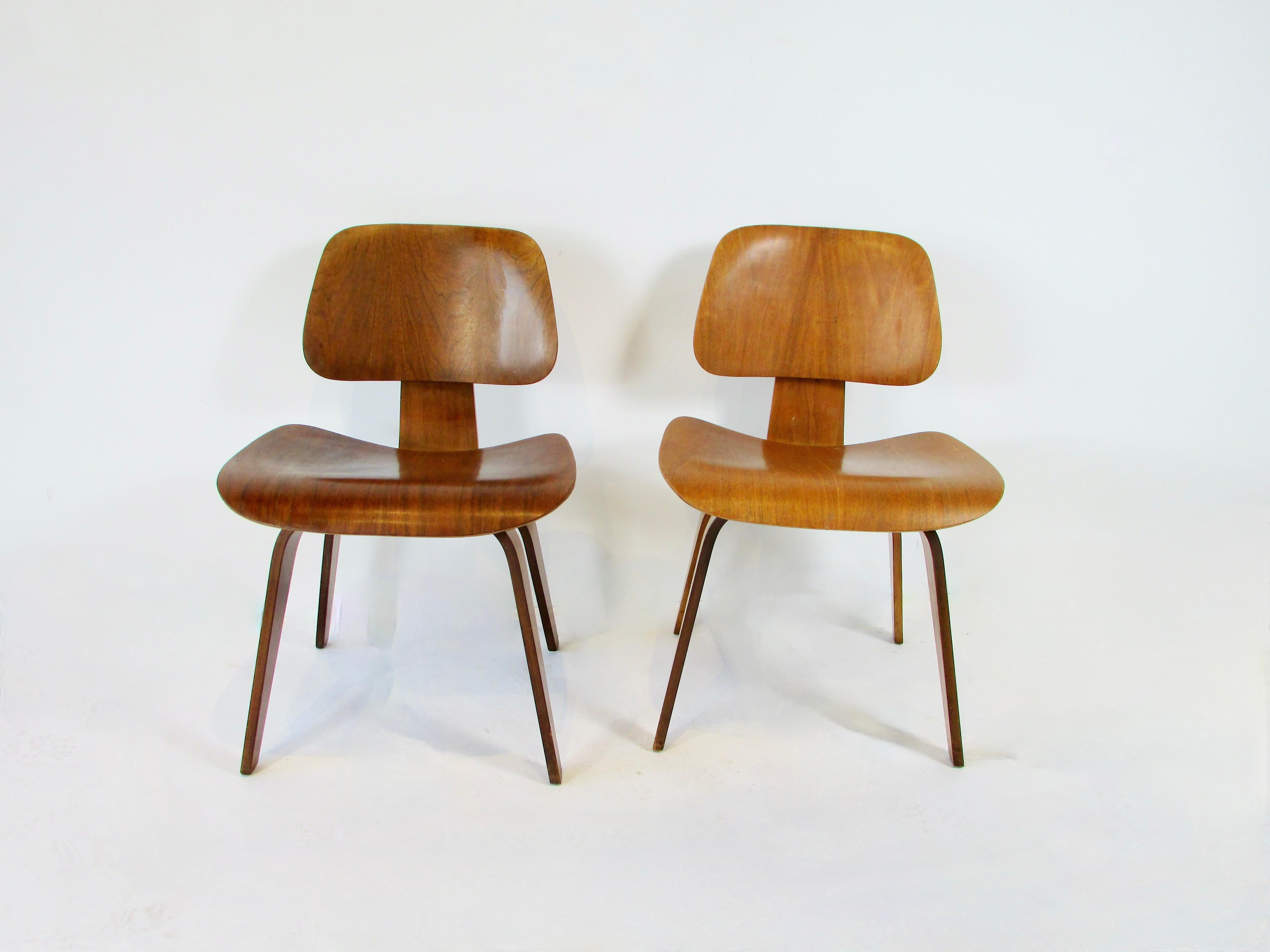Zwei Herman Miller DCW (dining chair wood) Stühle. Aus dem Studio für Bürodesign von Charles und Ray Eames . Beide Stühle sind in Nussbaum ausgeführt. Sie werden einzeln verrechnet. Nachlassfrisch in originaler, abgenutzter Ausführung. 