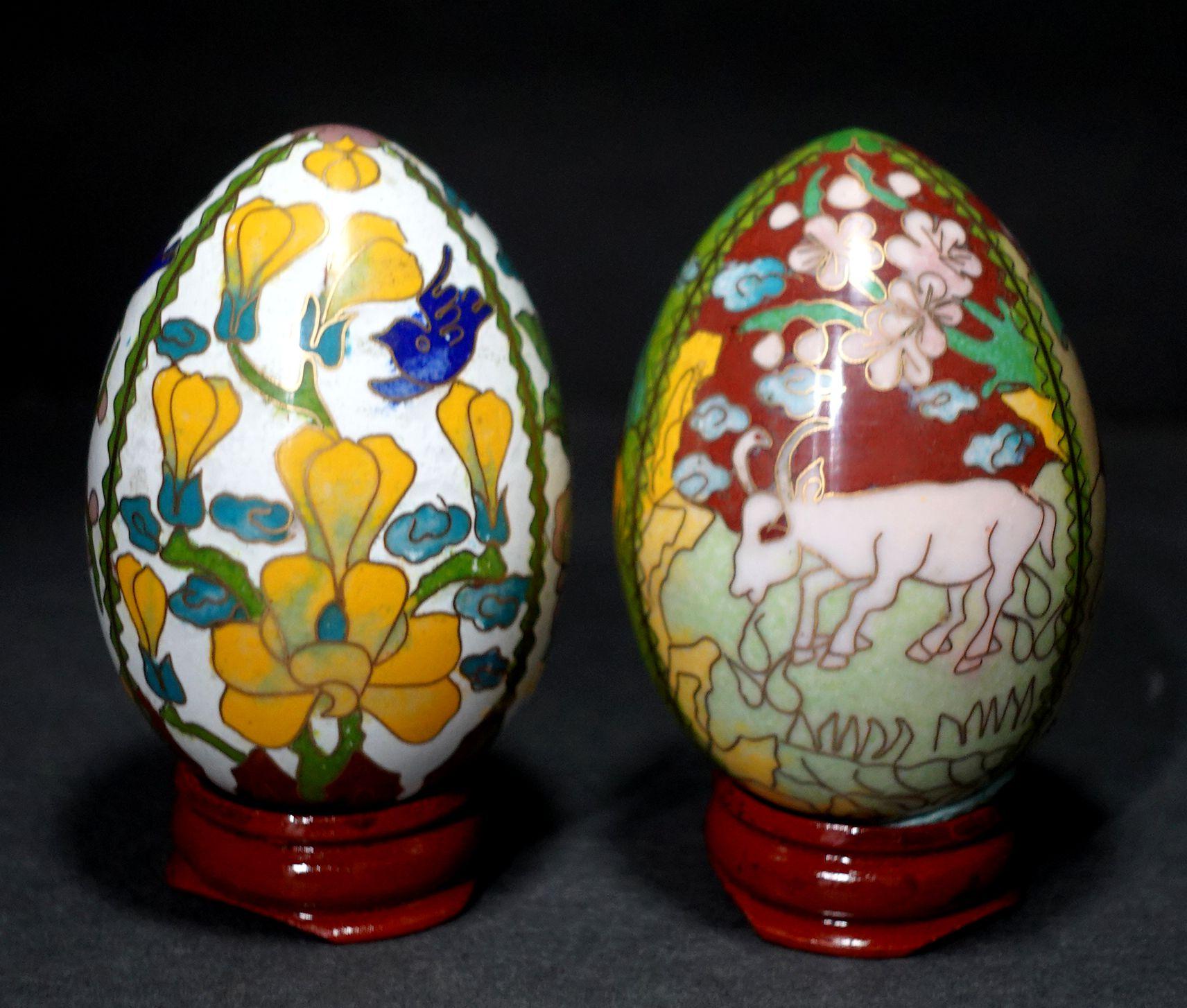 Presenting two beautiful Chinese cloisonné enamel eggs depicting flowers and animals with wood stands, early 20th century.