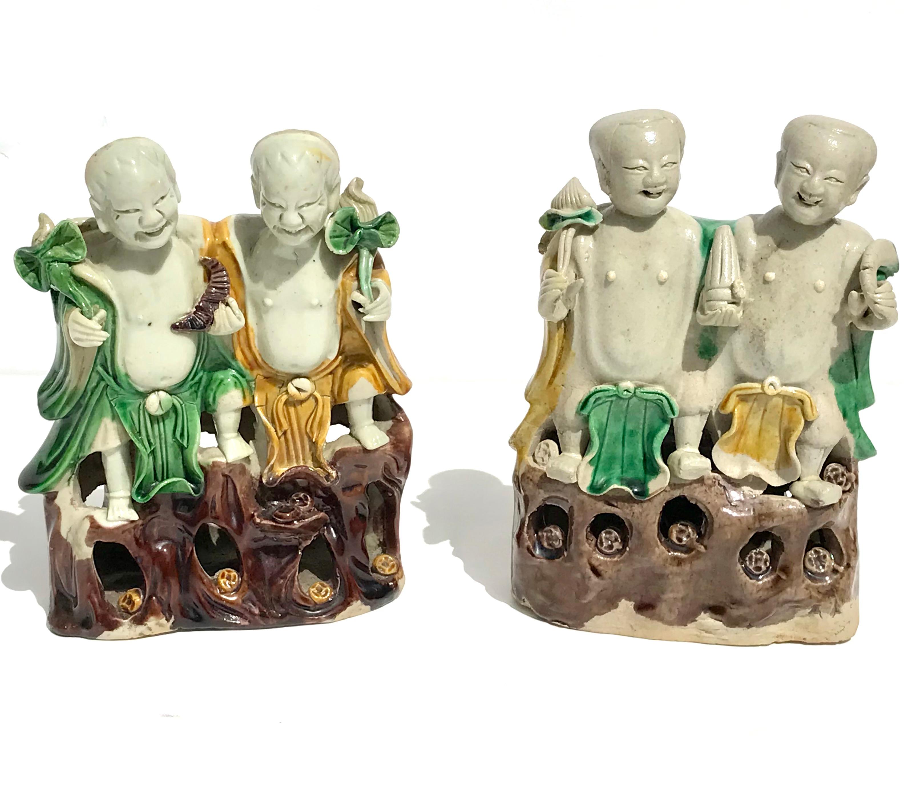 A Pair of Chinese famille verte laughing twins 'HeHe Erxian' biscuit group, Kangxi (1662-1722), the two boys with jovial expressions and seated upon an openwork rock-base studded with coins, the left-hand figure wearing brightly enamelled yellow