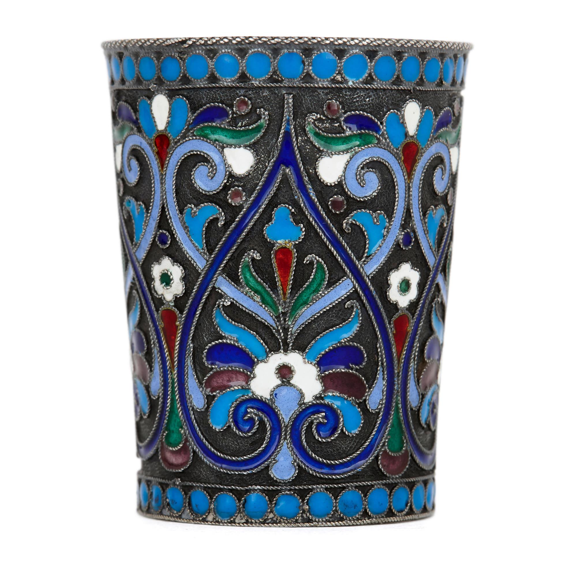 This matching pair of early 20th century Russian drinking cups (or vodka cups, also known as beakers) are made of solid silver. Cylindrical in form, the cups narrow slightly from the rim to the base. The cloisonné enamelwork of each cup is extensive