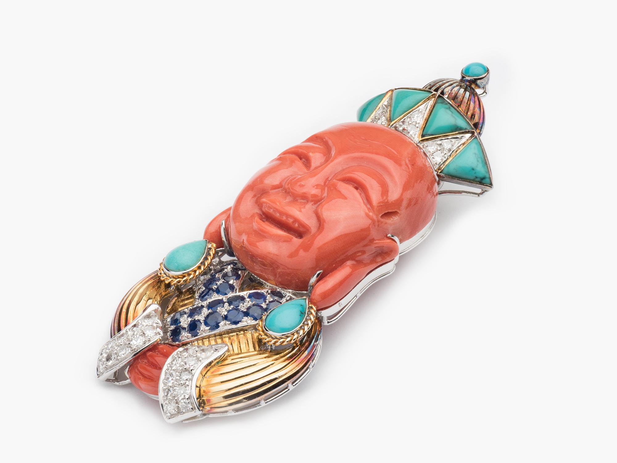 A laughing Buddha Clip Brooch with a carved Coral face accented with Turqouise, Sapphires and Diamonds set in 14k yellow and white gold.