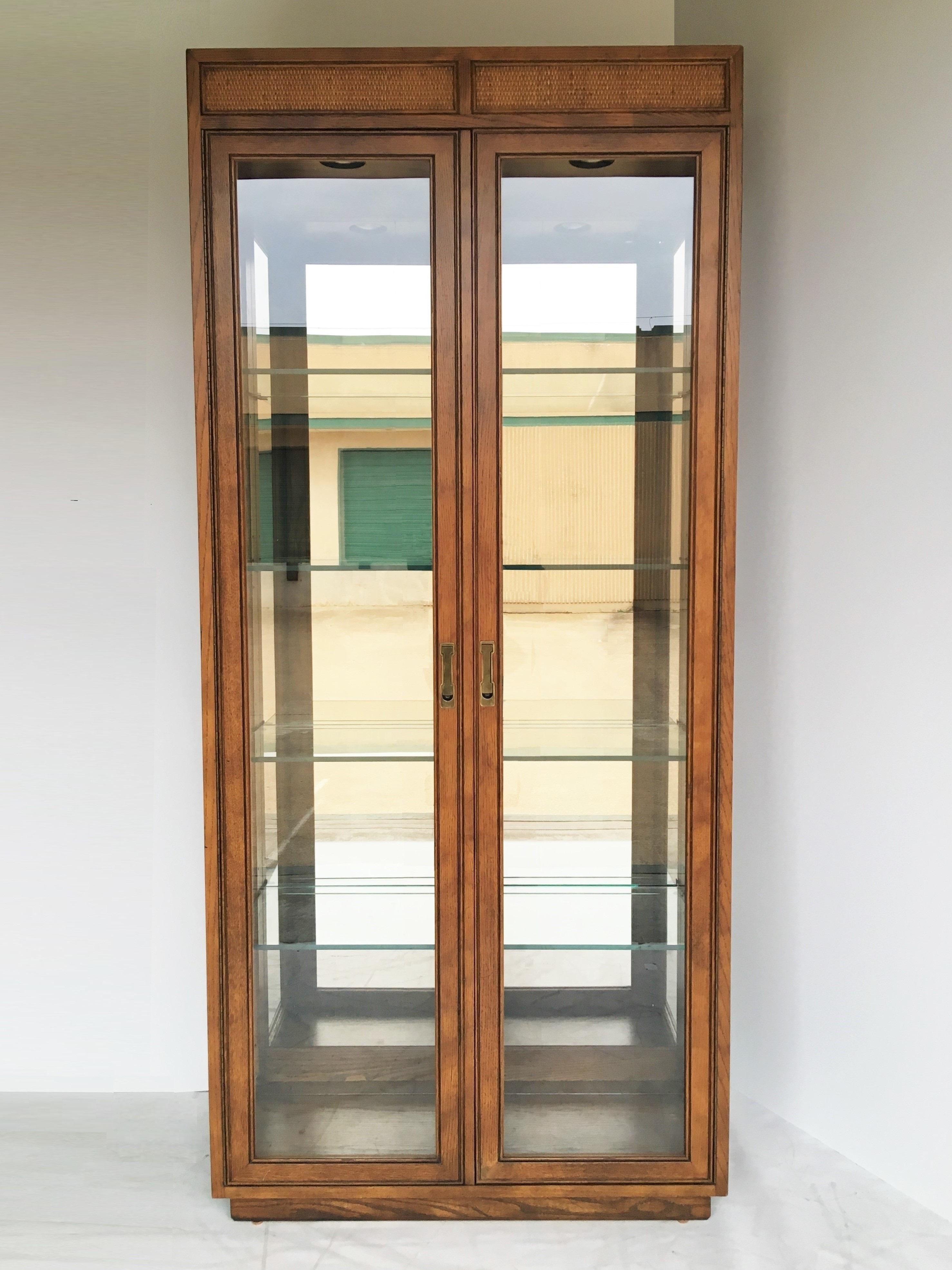 A great pair of Campaign style curio display cabinets. The cabinets feature two glass doors which open to an interior with a mirrored back. There are four thick glass shelves in each and two lights in the top. Brass hardware adorns the front.
 