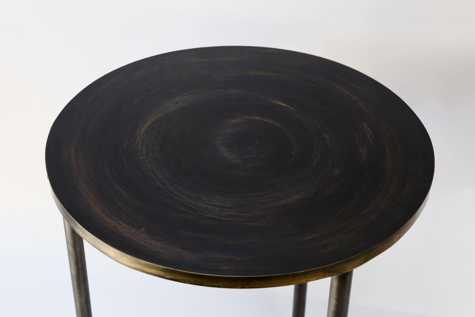 Custom steel and brass side table, table has a round brass top with a brass banded edge upon a three-legged steel base. Finish of top features light circular swirl design contrasting against a dark background.