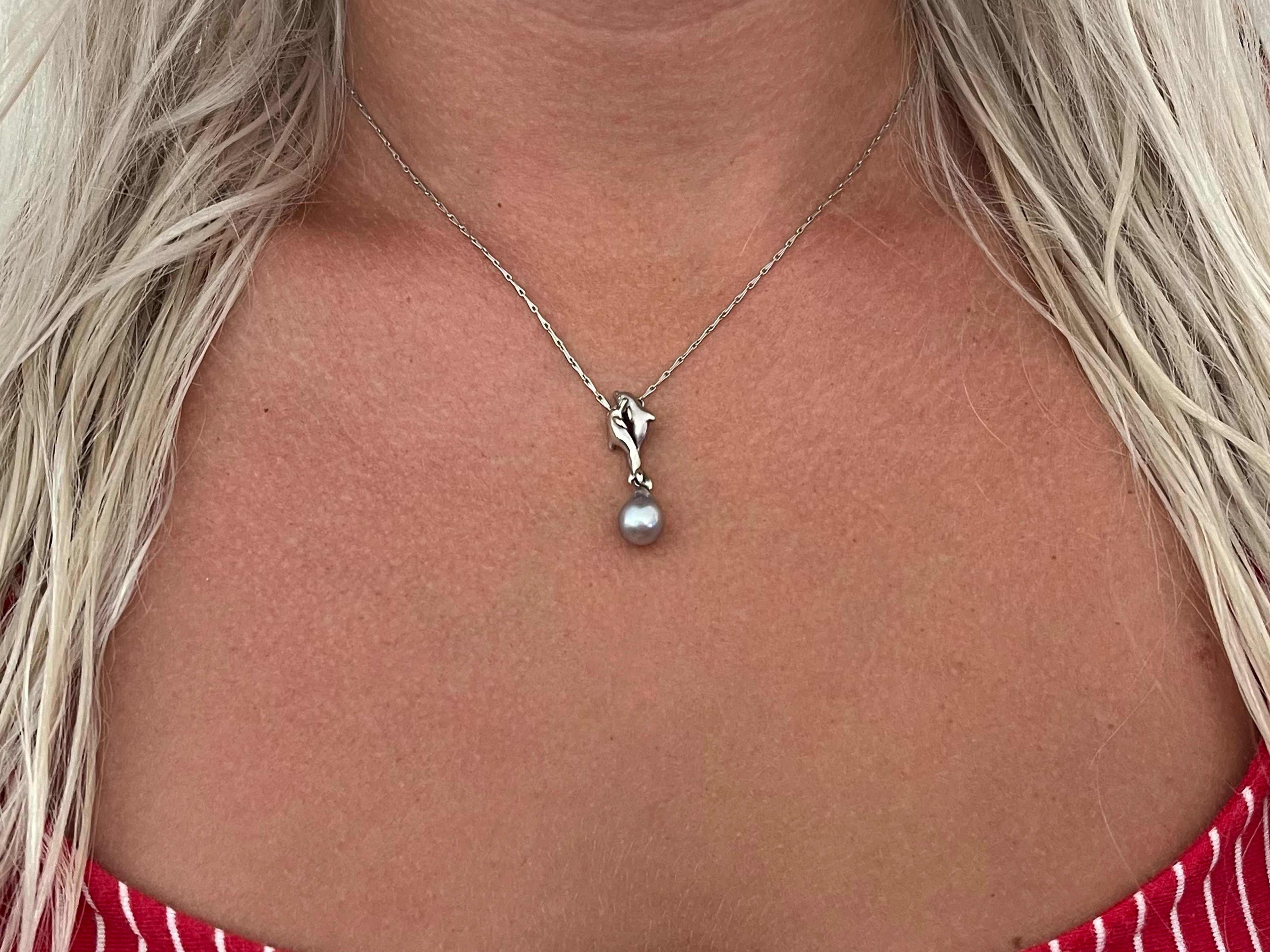 This pendant features two intertwined dolphins with a cultured silver pearl attached at the tail. The pearl measures 8 mm in diameter and the pendant drops 31 mm from the 16