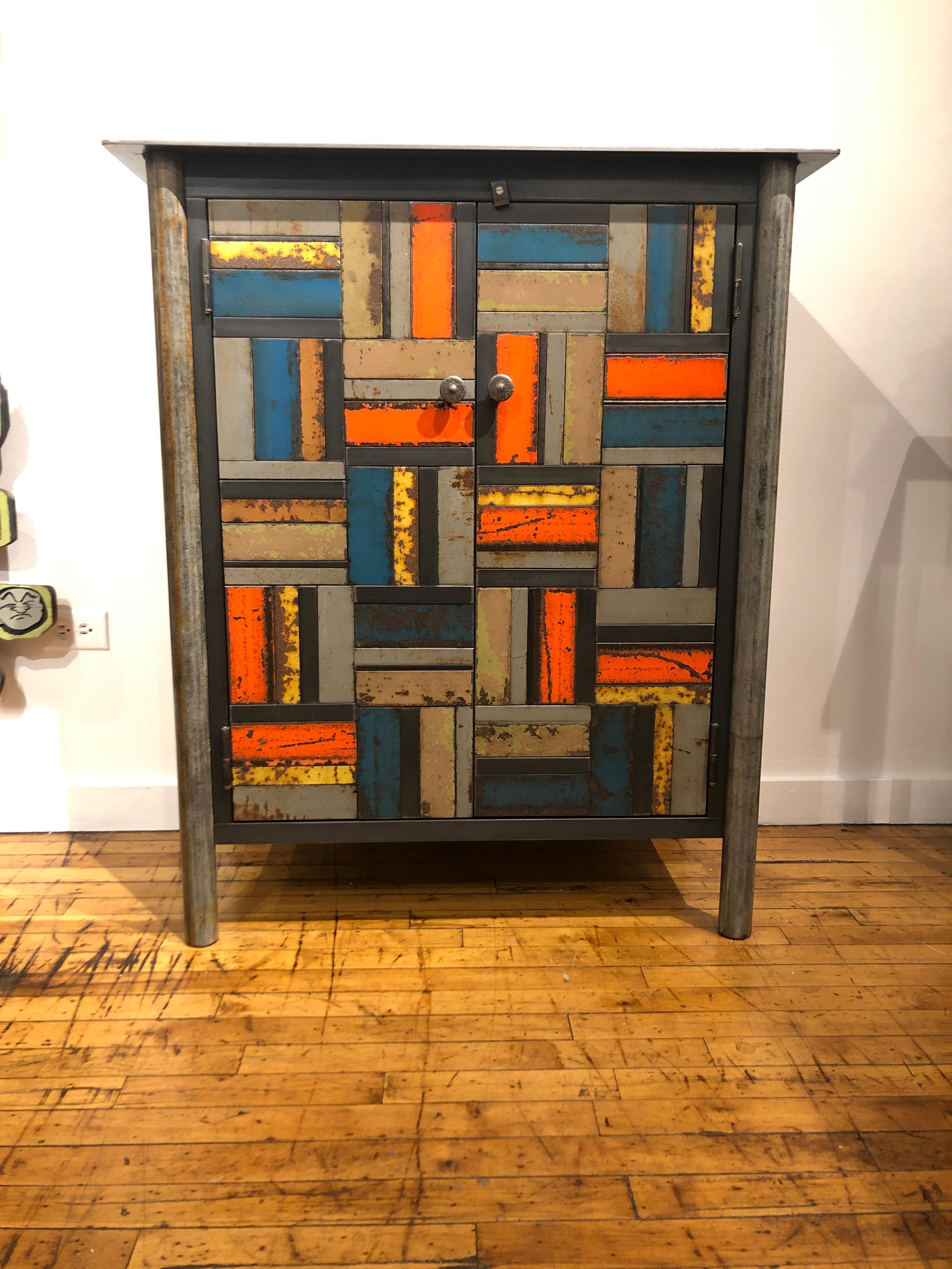 This is a totally functional two-door cupboard. It is created from hot rolled steel and found steel. The legs are made from salvaged pipe. The panels on the door fronts and sides are made from salvaged pieces of steel with the original paint and