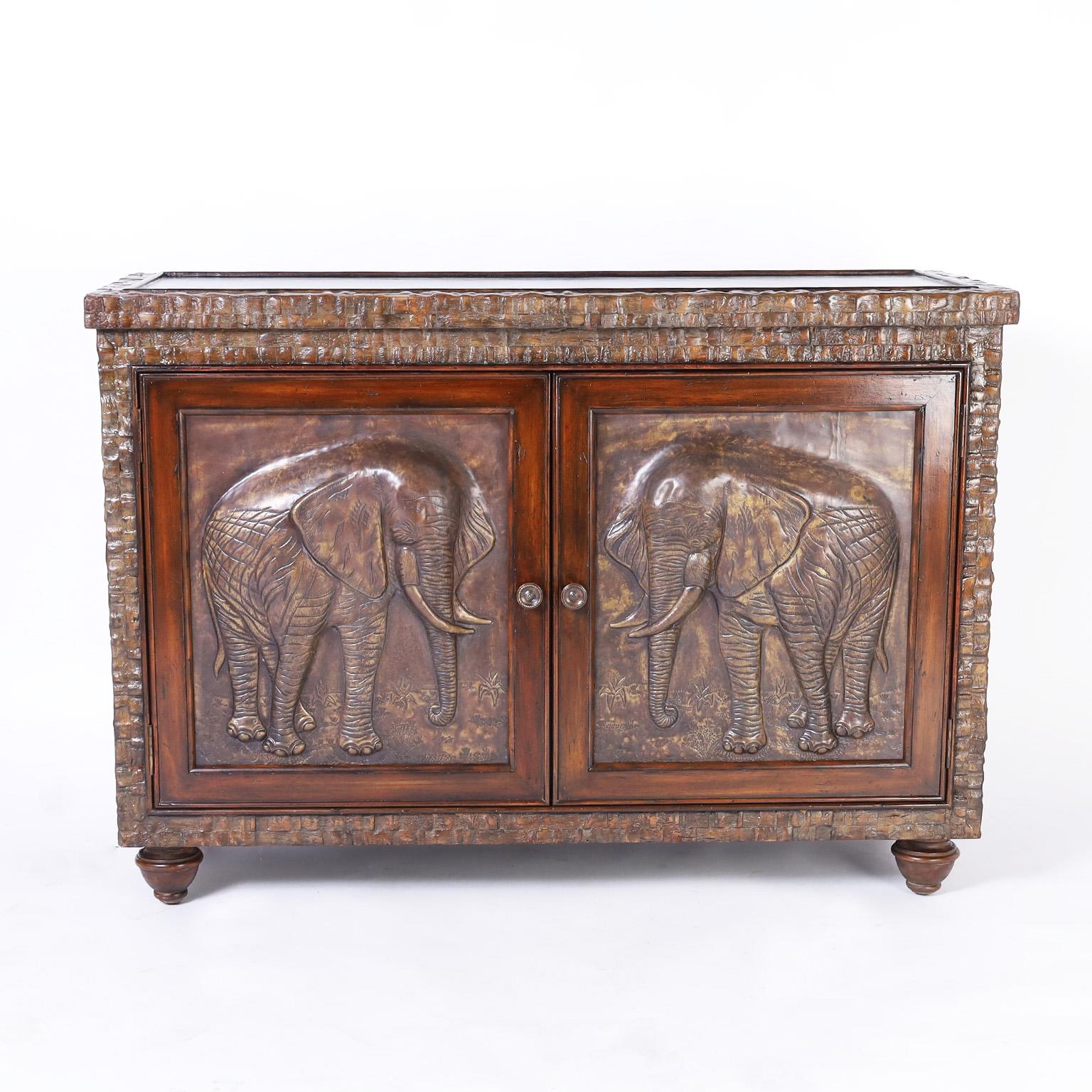 Handsome vintage British colonial style cabinet or chest with a polished coconut frame, featuring tooled leather top and sides, two mahogany doors with bronze elephant reliefs, mahogany interior with two drawers and turned feet. Signed