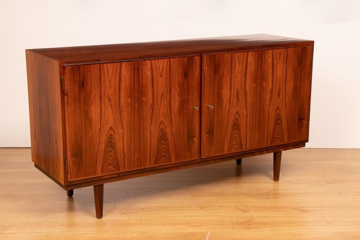 A midcentury sideboard in rosewood featuring a two-door front, internal tray drawers and storage shelf.