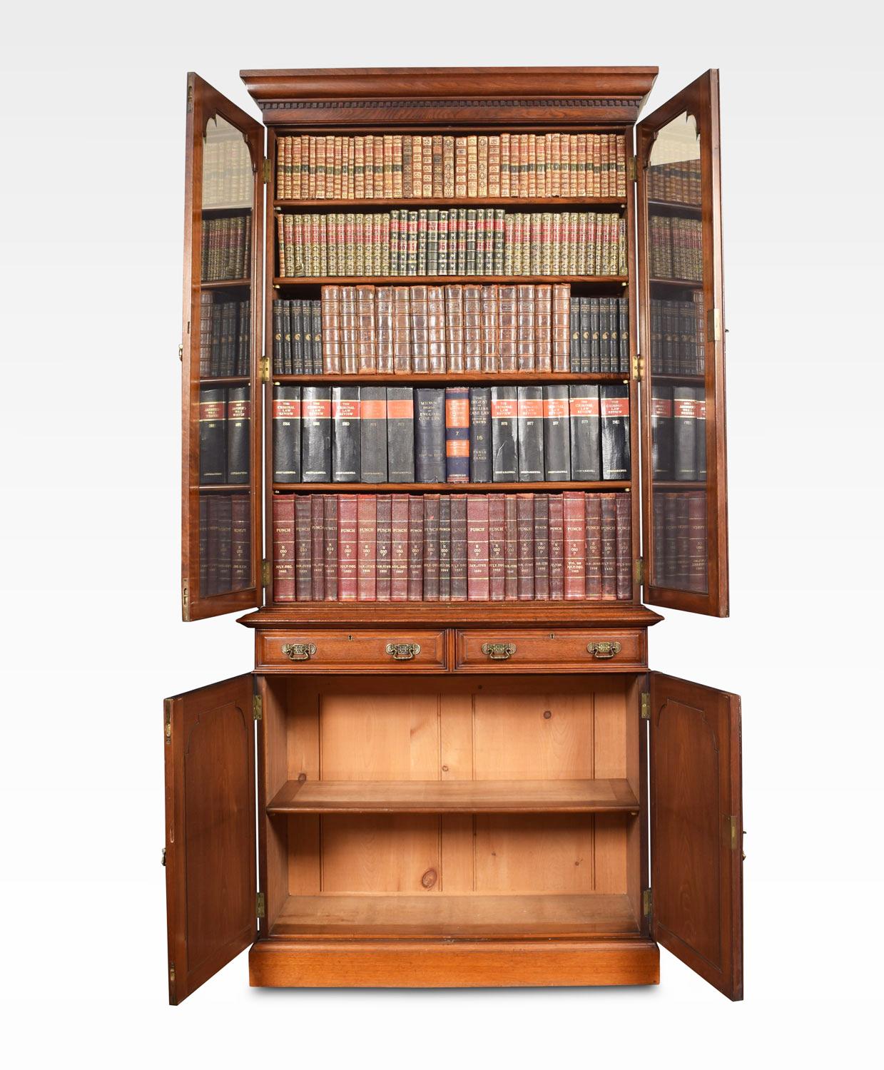 Walnut bookcase having flared moulded cornice over two beveled glazed doors enclosing four adjustable shelves. The protruding base having two short draws with brass handles. Above two paneled doors opening to reveal single shelf, all raised up on