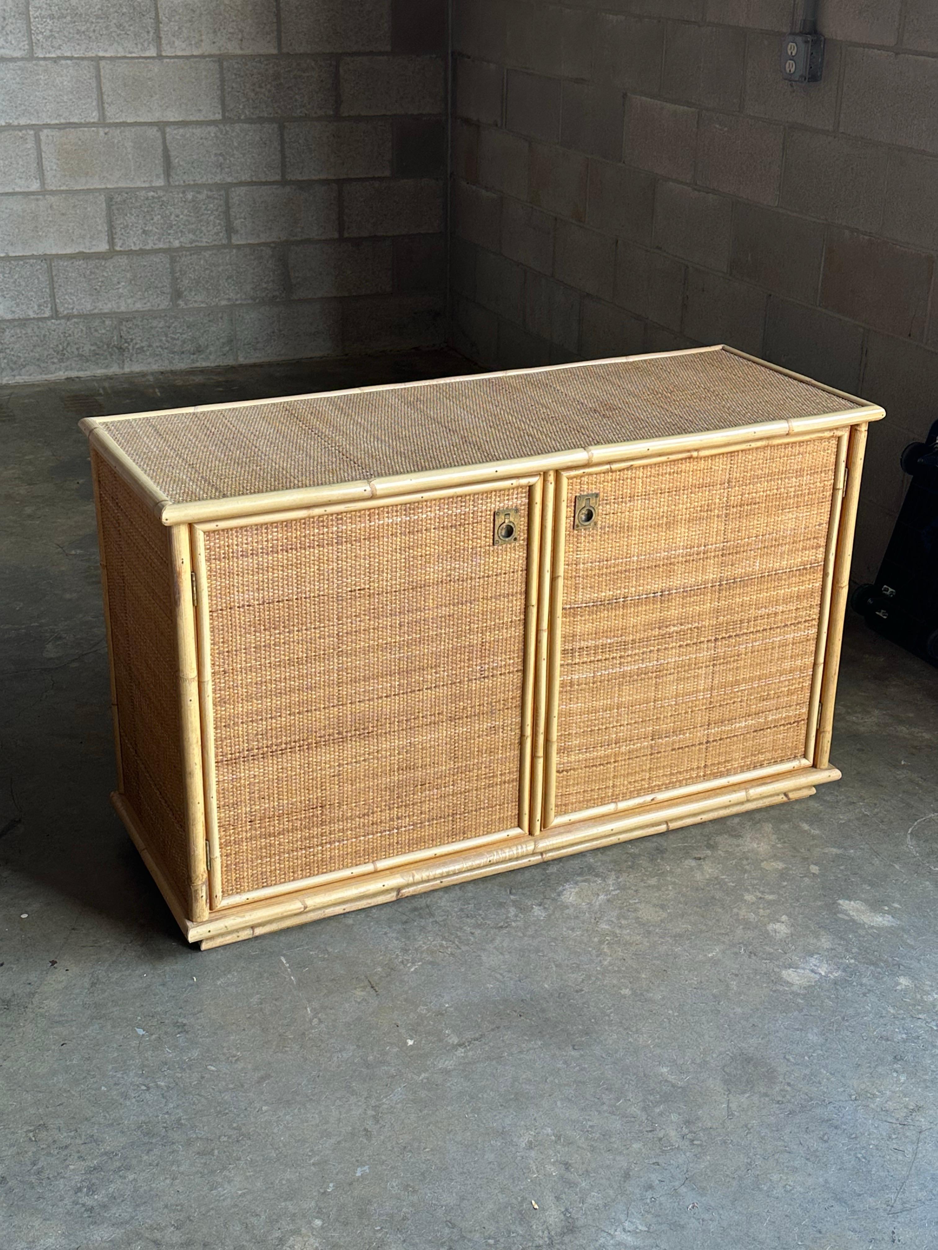 Una piccola credenza o mobile prodotto da Del Vera in Italia intorno agli anni Settanta. Ottima struttura in bambù con piani, lati e fronte rivestiti in rattan. Belle maniglie in ottone. L'interno è dotato di un ripiano su entrambi i lati 