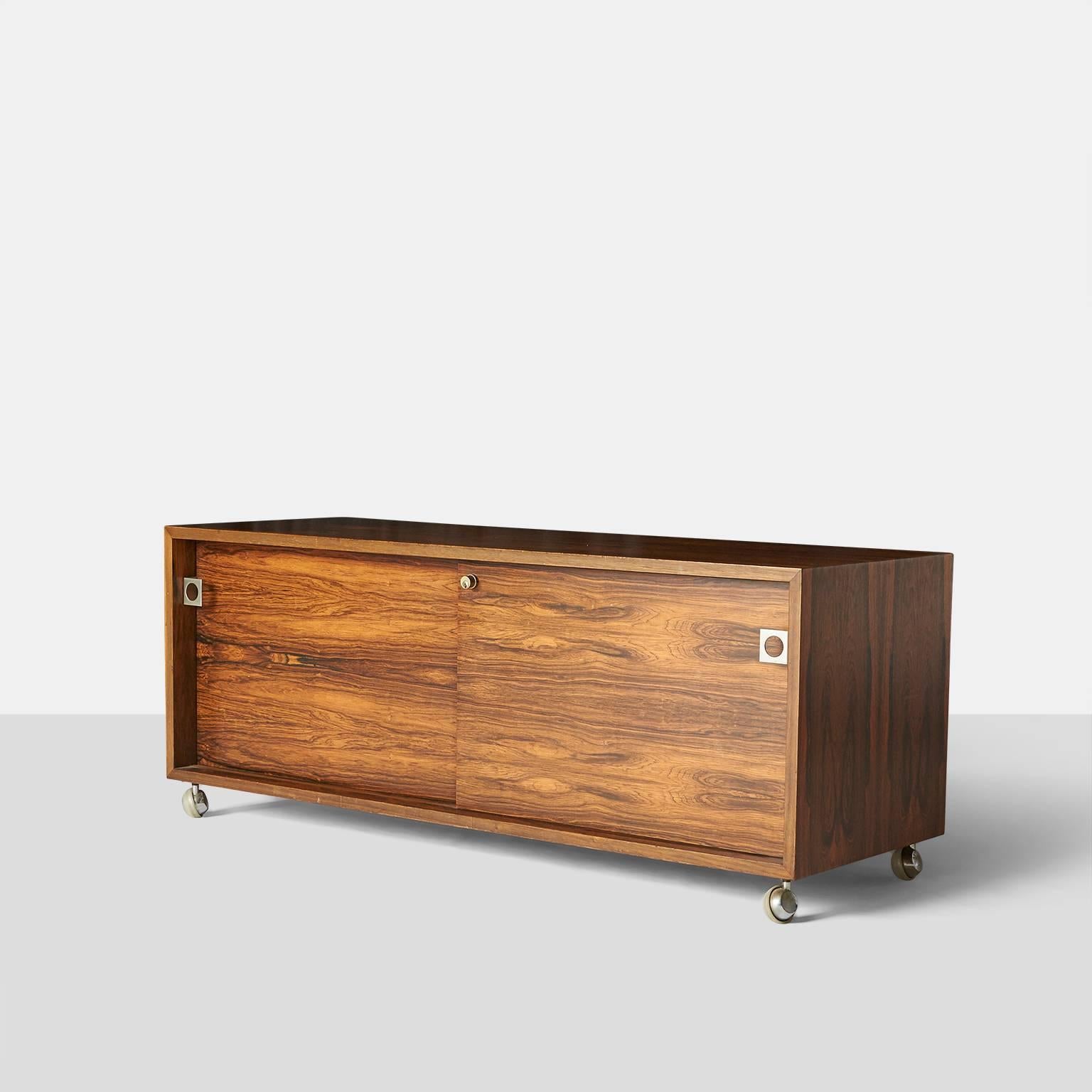 Storage cabinet by Bodil Kjaer.
A storage cabinet in rosewood with two bypassing doors and an adjustable shelf on each side. The rosewood cabinet has four casters, steel square form door pulls, and a lock for the doors. Produced by E. Pedersen &