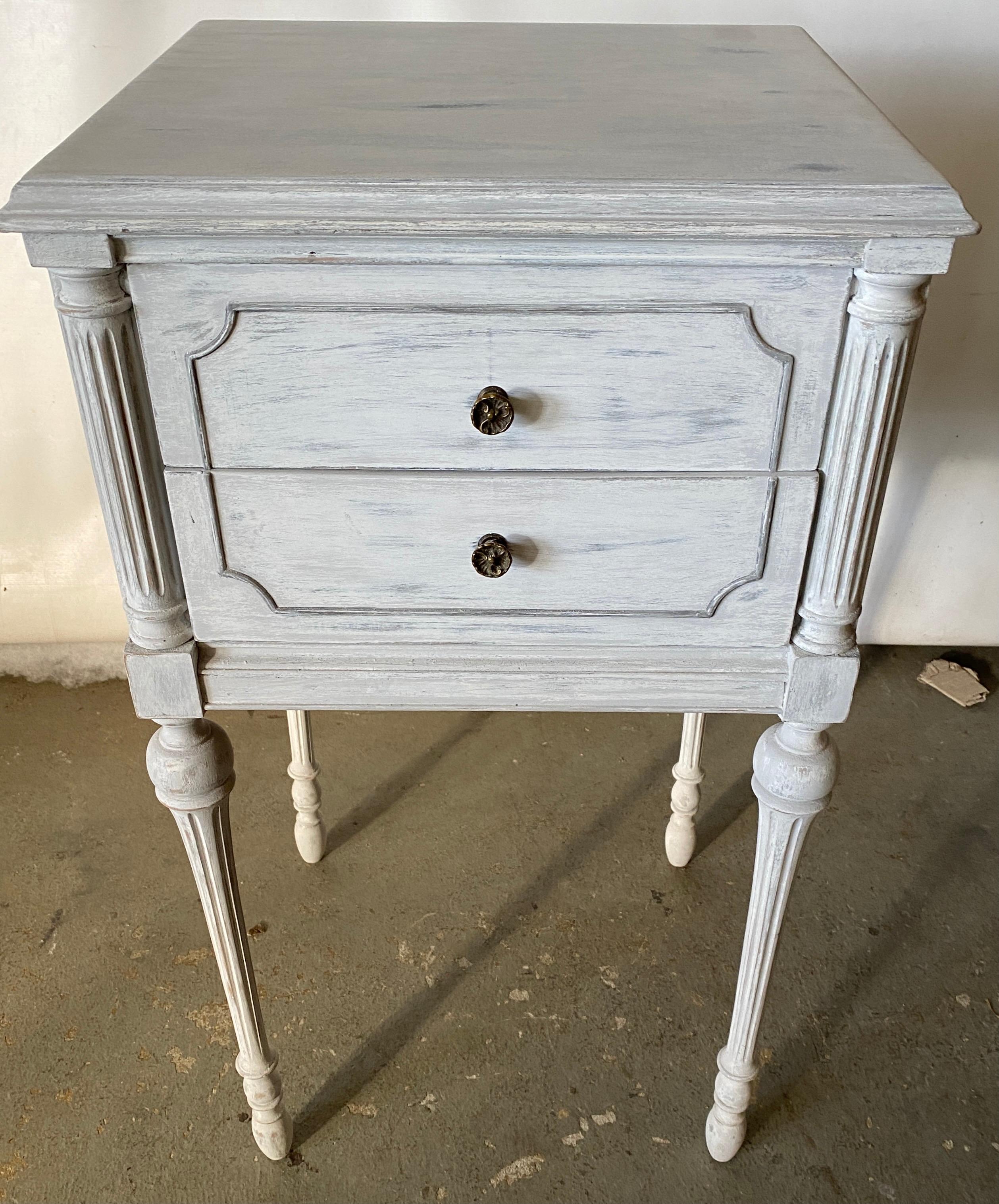 The grey and gold gilt painted metal night stand has an open upper shelf with a pull out tray with a cubby hole or lower shelf for more storage. This night table or stand will fill the bill if you are searching for a Swedish Gustavian, neoclassical