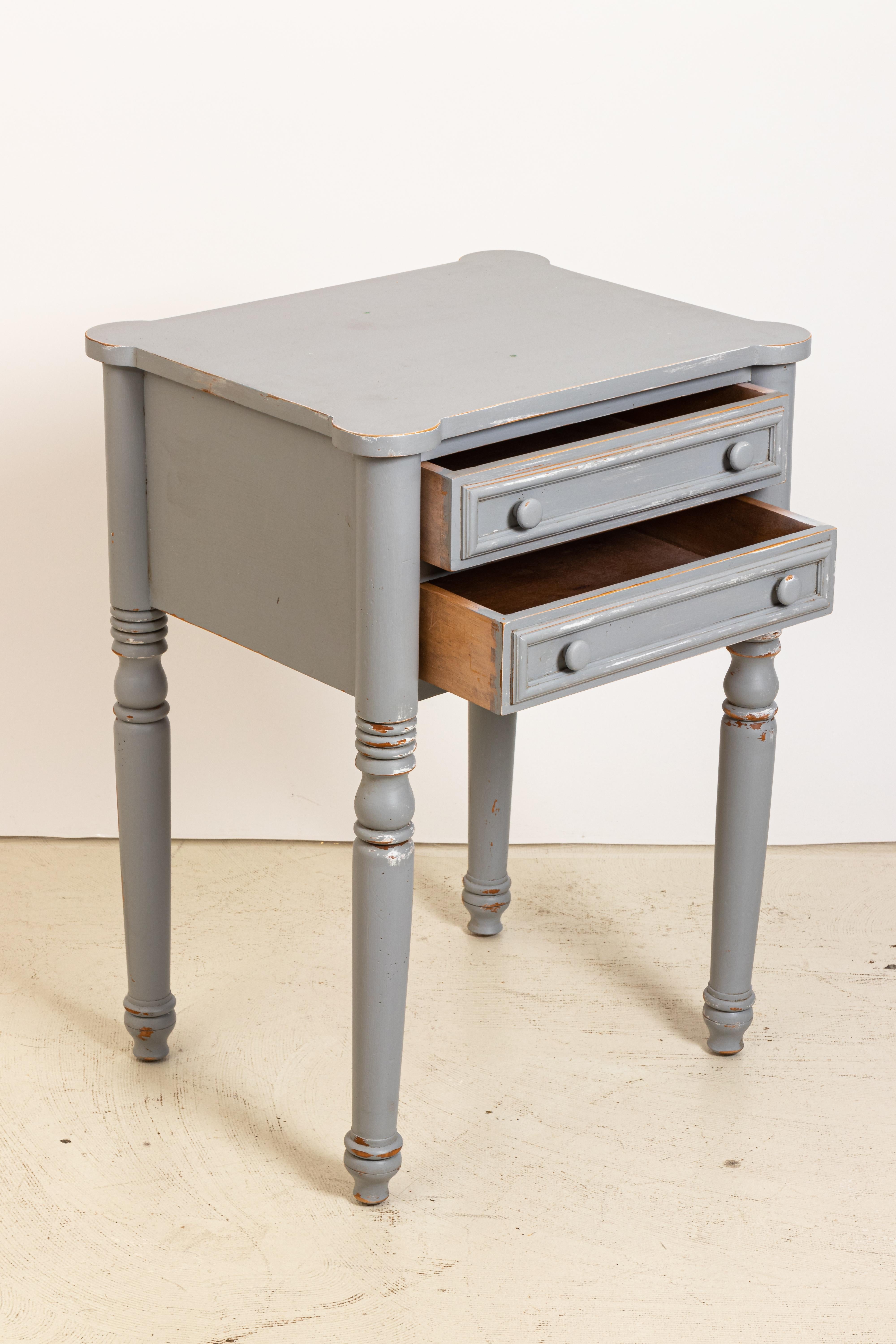 Grey painted two-drawer pine table with cookie cutter corners in a distressed finish, circa 1970s-1980s. Some wear to the painted finish. There is also evidence of finish loss. Made in the United States.
