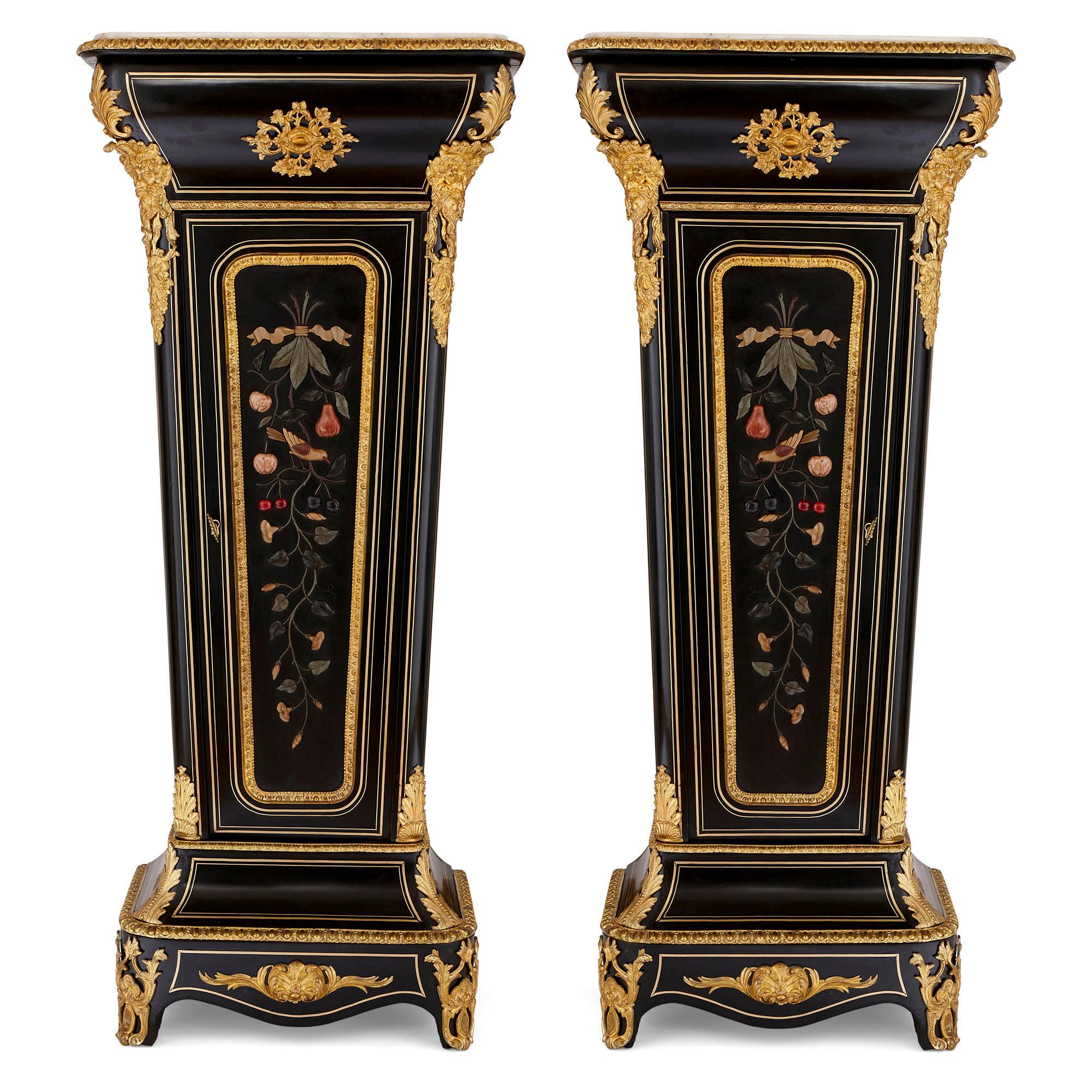 These pedestal-cabinets are sophisticated pieces of antique French furniture. They are crafted from ebonised wood which is inlaid with brass and mounted with decorative gilt bronze (ormolu) motifs and hardstone designs. 

The pedestals are of