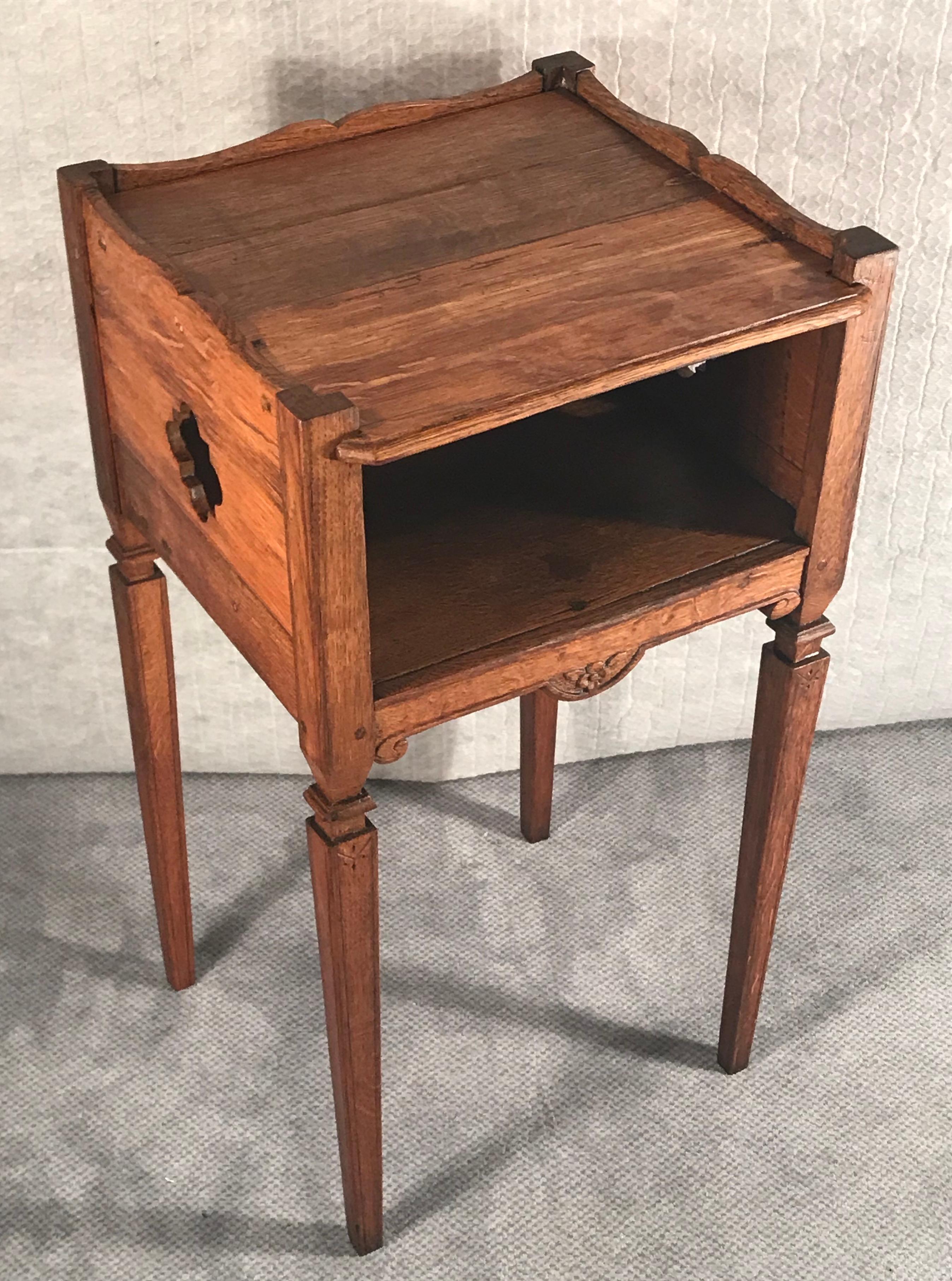 Two French provincial Baroque style bed side tables or nightstands. 
The farm style tables date back to around 1800. They are made of massif oak wood and have some very pretty carved decorations. Both of them have an open compartment with an open