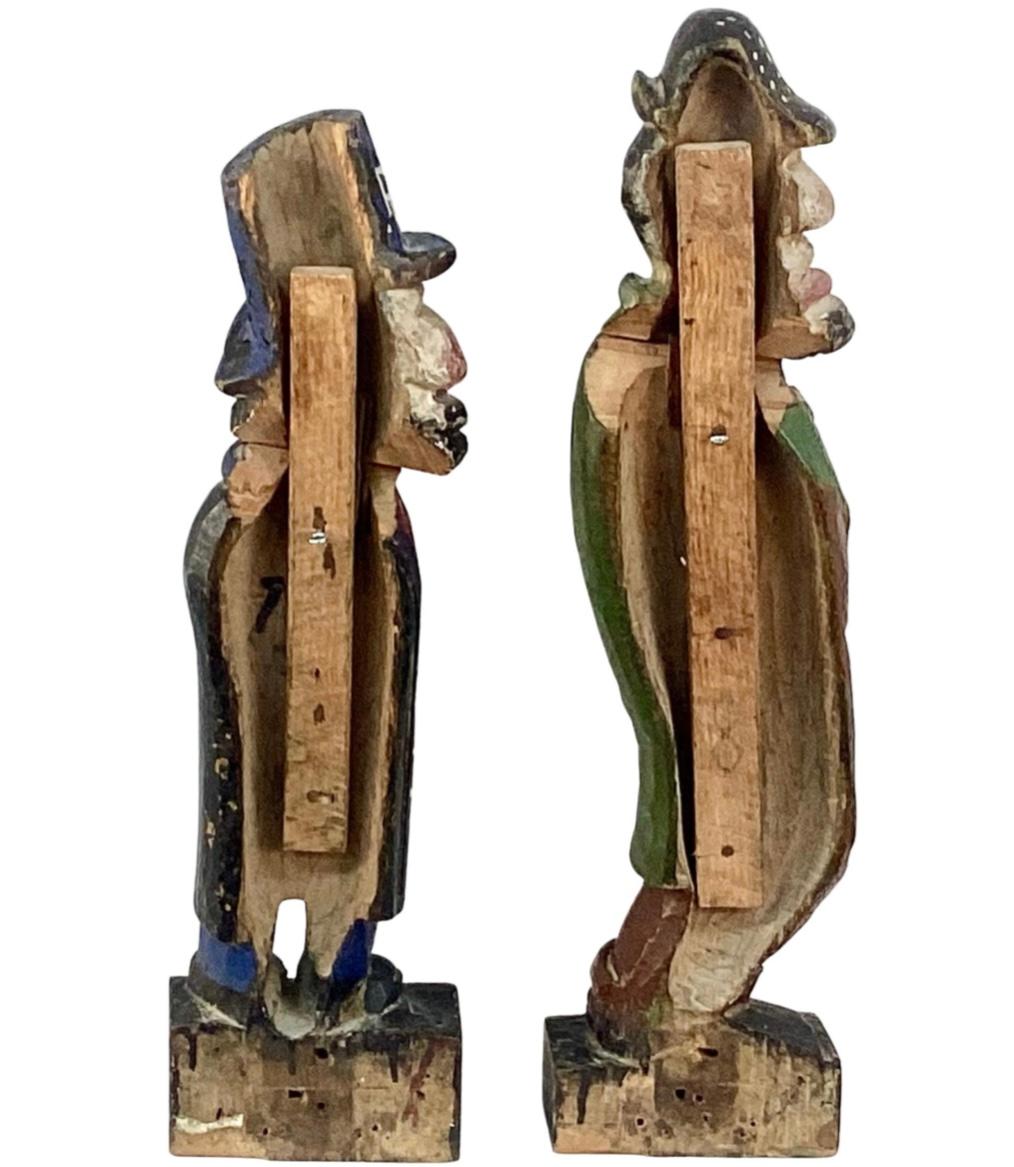 A very rare pair of late 19th century folk art carved wooden carnival knock down gallery targets. Both are of males in long coats, trousers, shoes, and hats. Slightly Movable heads connected to leather hinges, with restored wooden brackets on