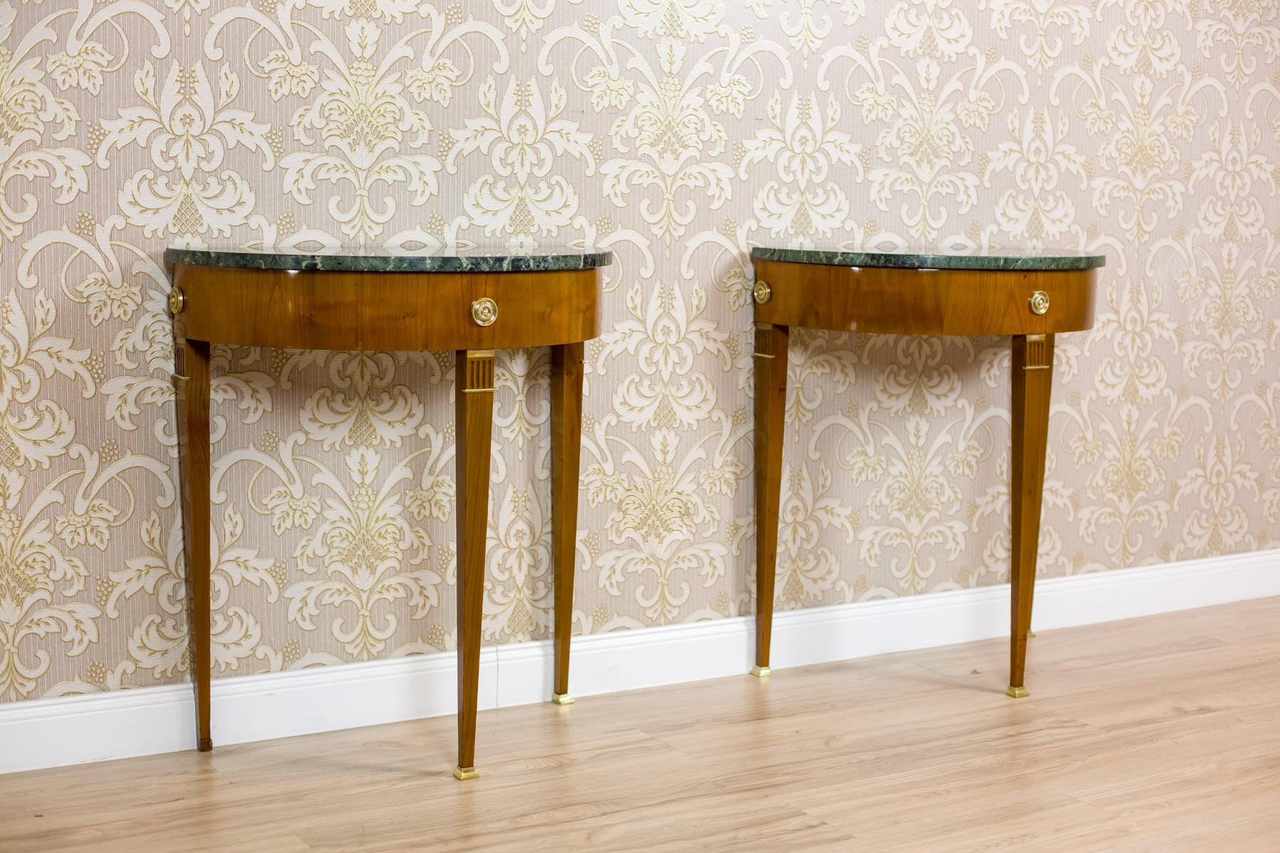 We present you this pair of wall tables, also called console tables, with marble tops in the shape of a semicircle.
The wide molding under the top is ornamented with brass rosettes on the line of legs.
Furthermore, the legs narrow towards the