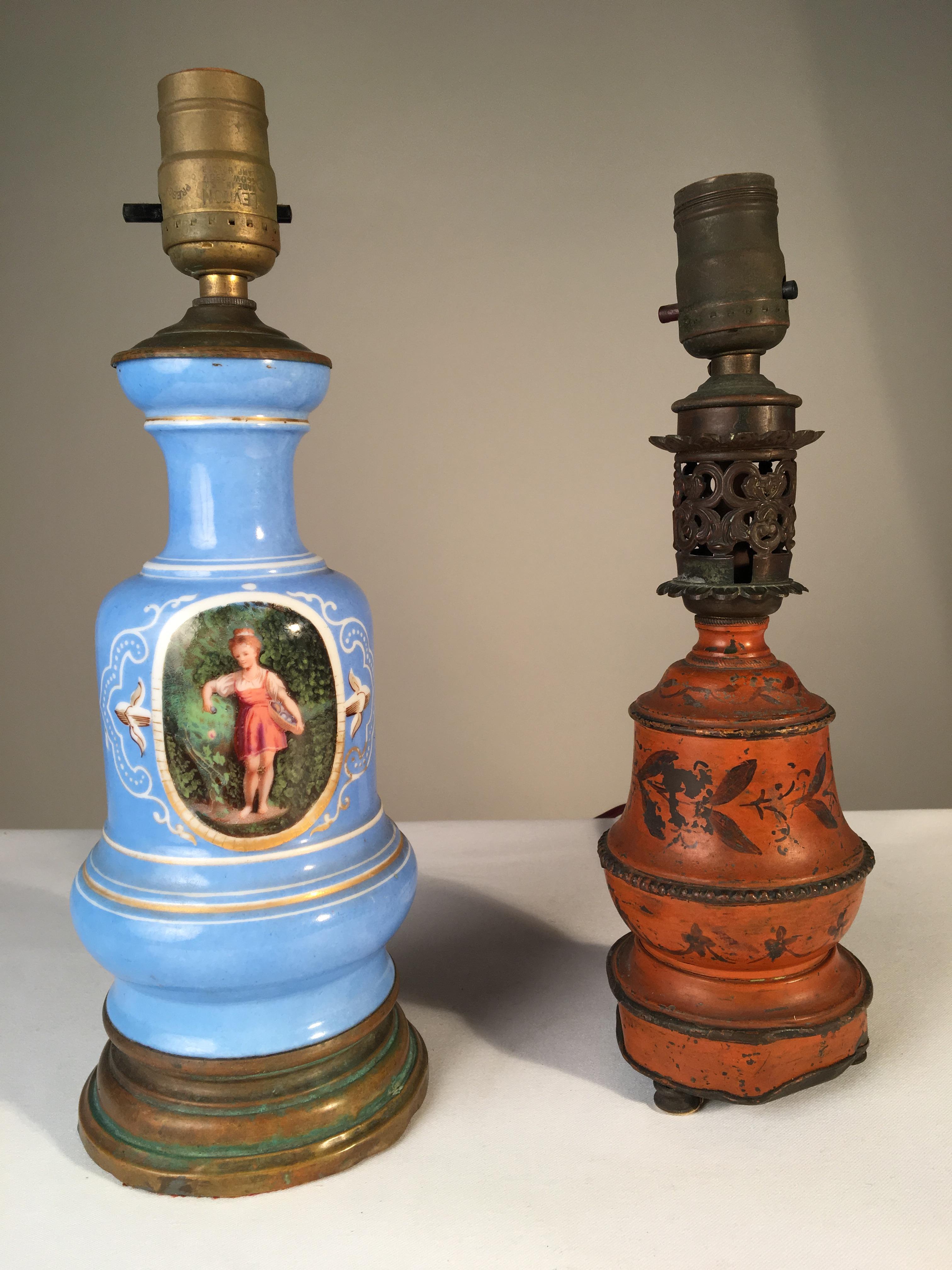 Two antique French table lamps, one blue porcelain with painted classical figure in a central cartouche, and the other a small tole lamp in a dark orange painted finish, both converted from earlier oil lamps.