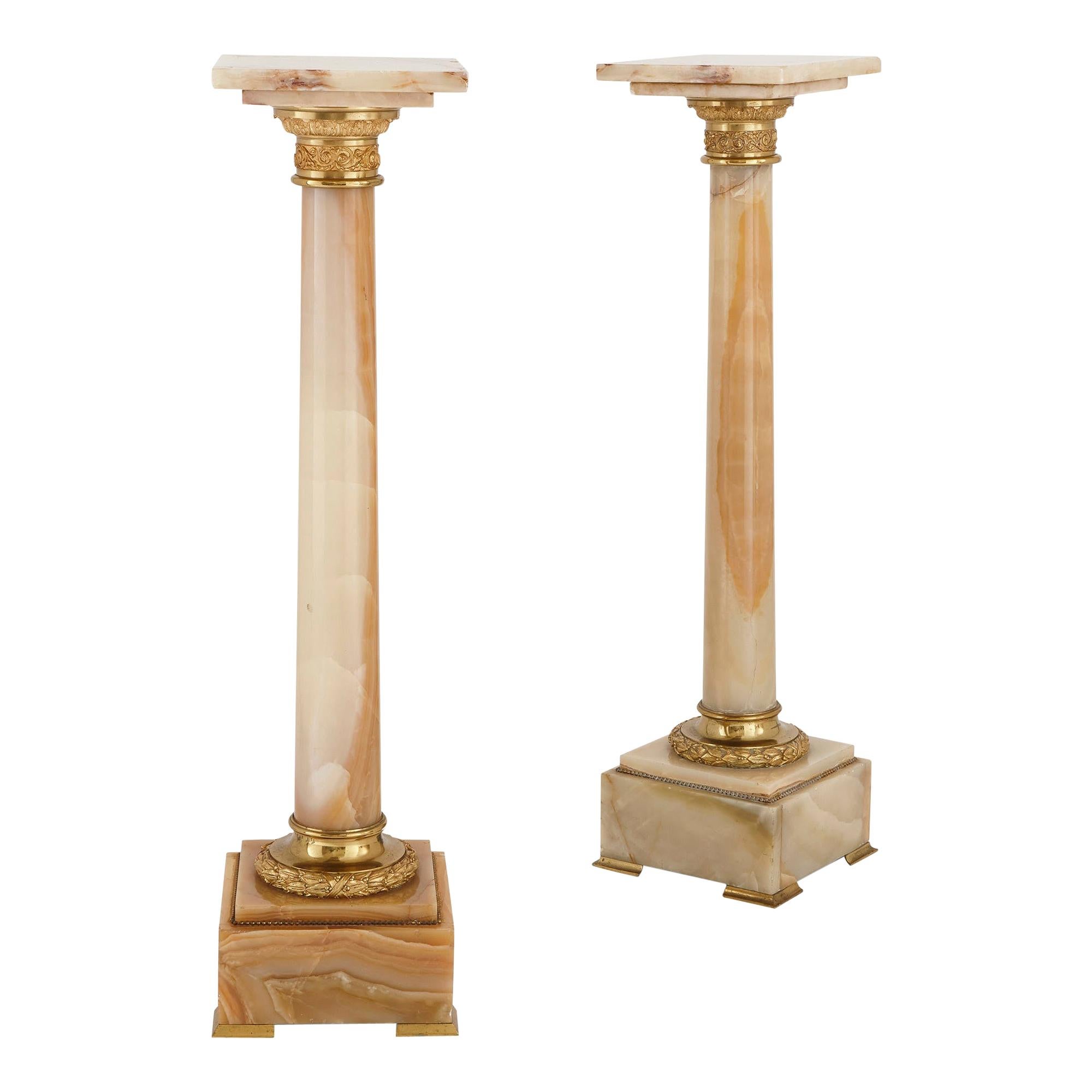 Deux supports français en forme de colonne en onyx blanc et bronze doré