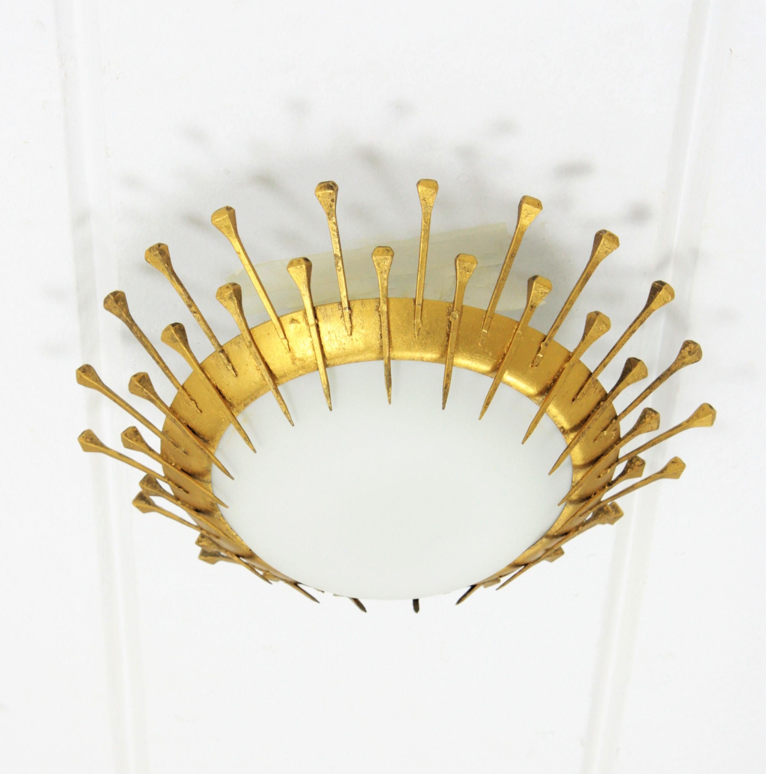 A pair of hand-hammered iron and opaline glass sunburst flush mounts with nails decoration and gold leaf finish. Beautiful pieces to place alone but also interesting mixed with other light fixtures in this manner to create a ceiling or a wall