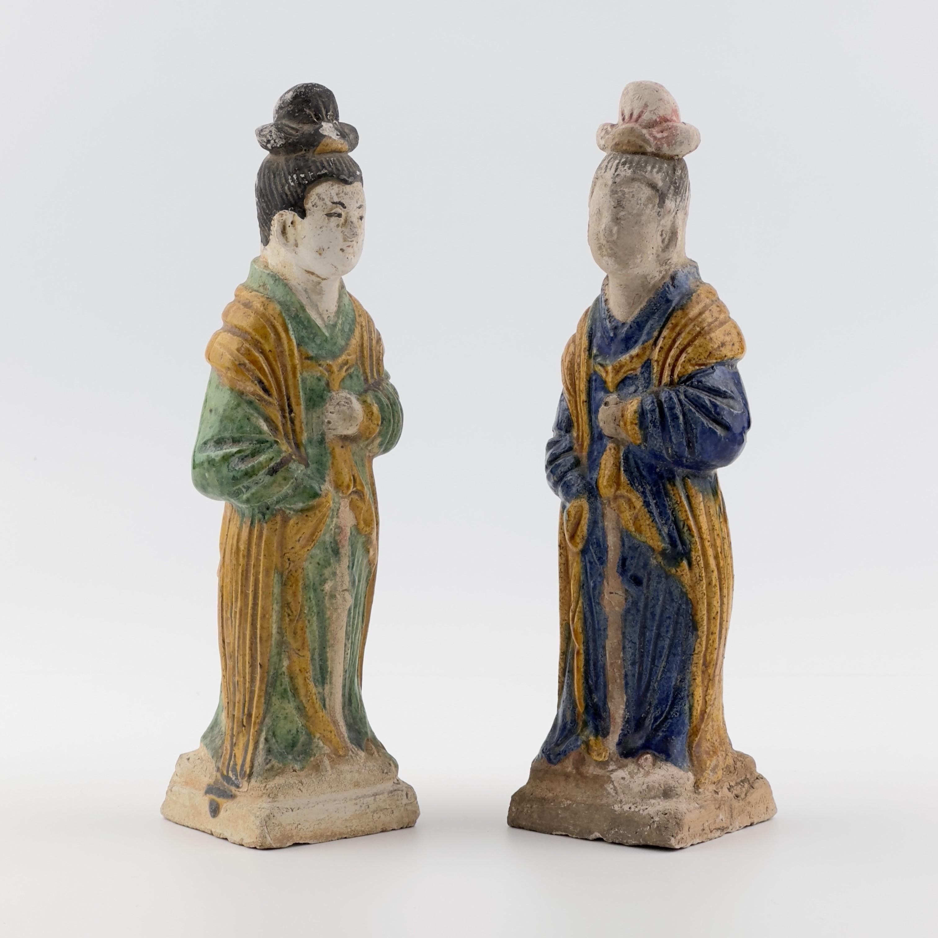 Two finely hollow-moulded terracotta statuettes from ancient China, dating to the Ming Dynasty. The figure is depicted standing, dressed in long, flowing robes, painted in vibrant blue or green and deep amber yellow. The hair is styled into an