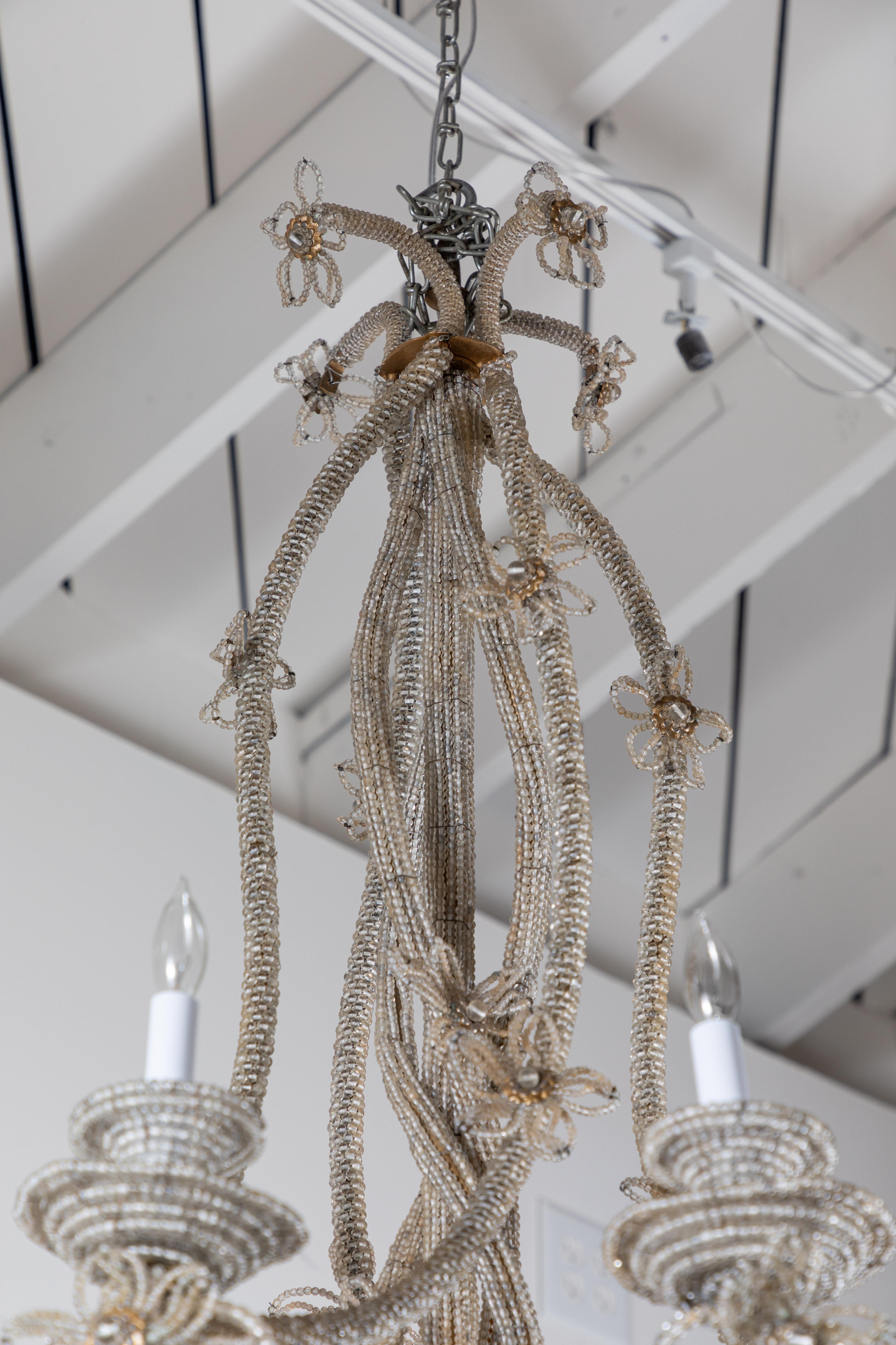 A pair of ravishing, unusual, hand-beaded, chandeliers with wonderful, twisting central column radiating to eight arms. The whole embellished by open leaf forms, flowers, and two-tiered bobeche.