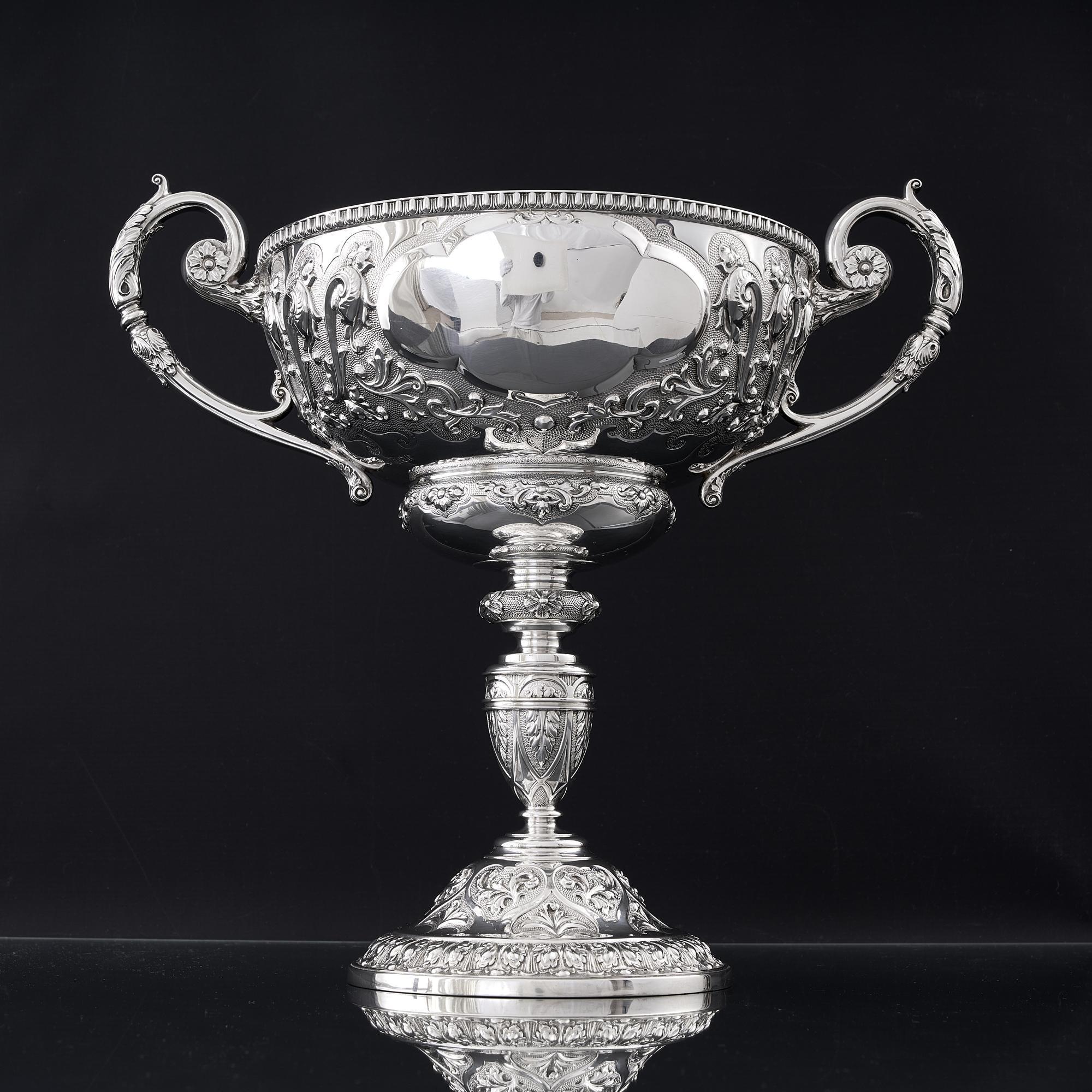 A magnificent late Victorian period antique sterling silver trophy. The wide shallow bowl, stem and base are all hand chased in high relief with various scrolling foliage and acanthus leaves set against a mottled background. The rim and base feature