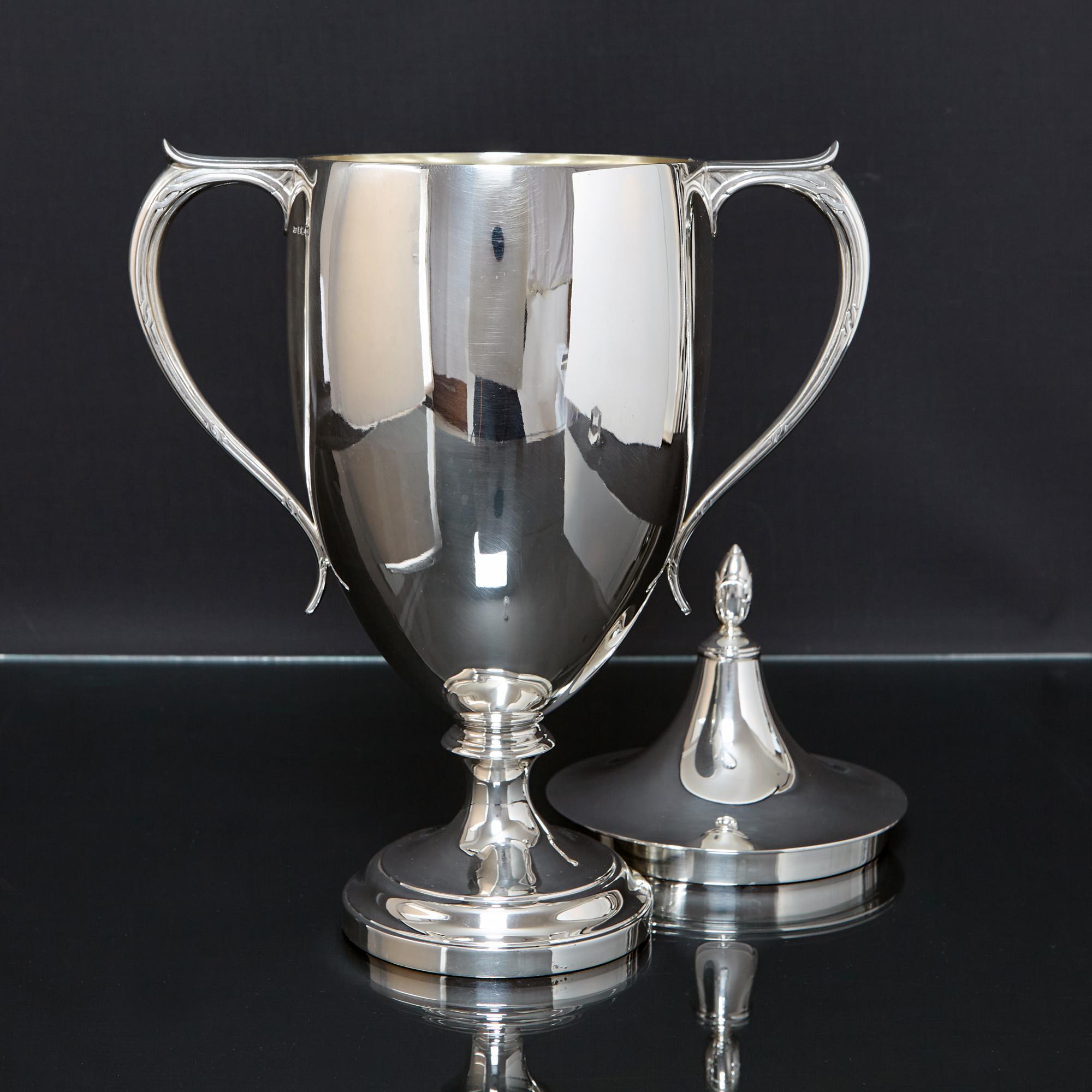 Stylish two-handled silver trophy cup and cover made in the Art Deco style and of the era. The silver trophy's elegant sweeping handles and finial are decorated with simple interwoven ribbons; a nod to the Art Deco period, making this a really