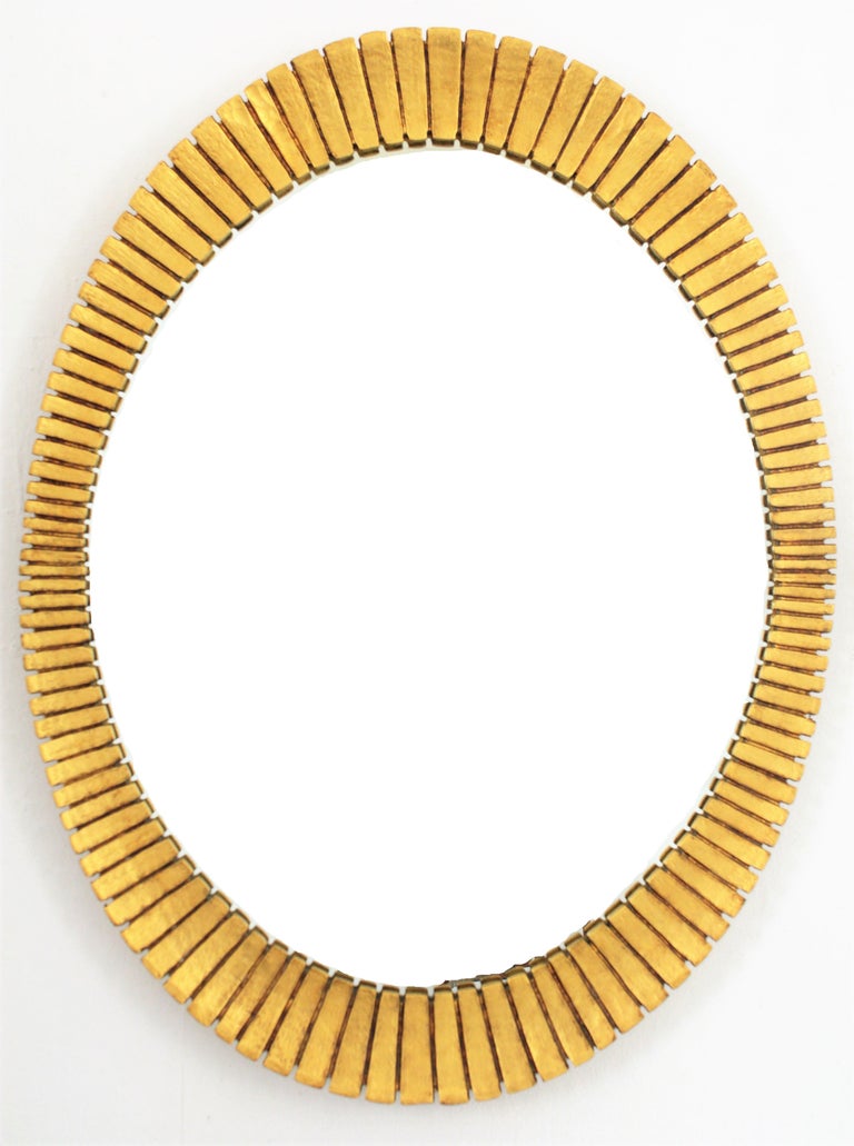Gorgeous scalloped giltwood oval mirrors with gold leaf finish in the Hollywood Regency style manufactured by the Spanish cabinet maker Francisco Hurtado. Ovoid shape frame with finely carved stripes and scalloped edge that make this mirrors highly