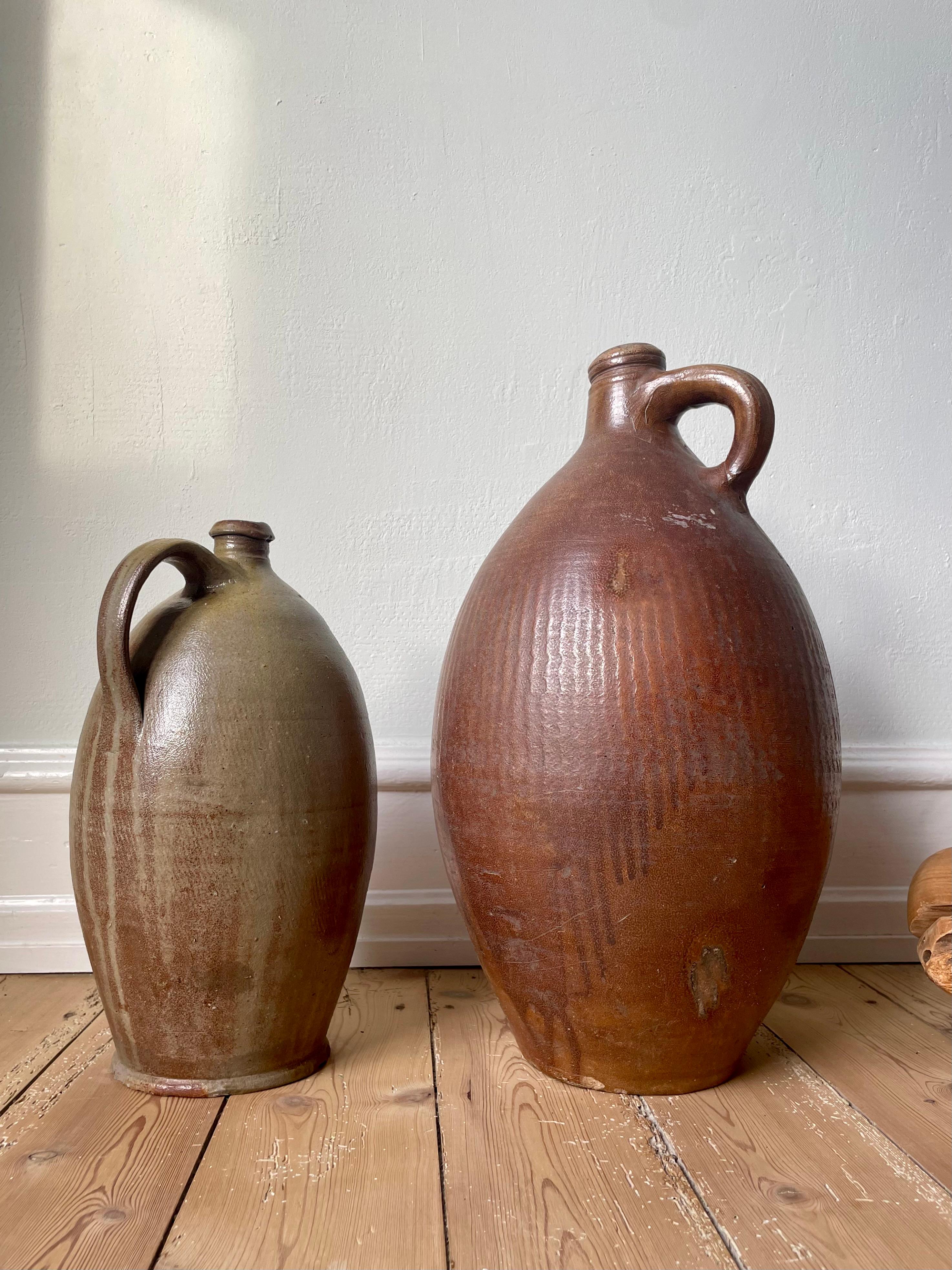 Pair of large authentic 19th century glazed terracotta pitcher bottle jugs originally used for containing water and olive oil - the smallest one still has the original cork stopper in the spout. Beautifully aged and weathered with stunning glaze in