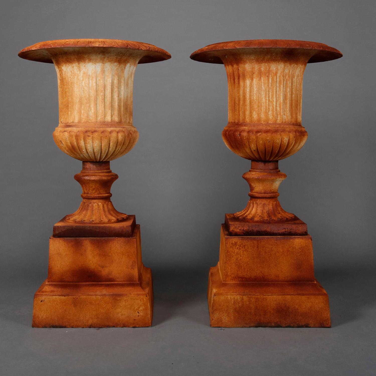 A pair of well cast French classical garden planters feature iron construction in pedestal urn form having melon bowls with egg and dart rims raised on central pedestals and seated on plinths, painted white with rust patina, 20th century.

Measures: