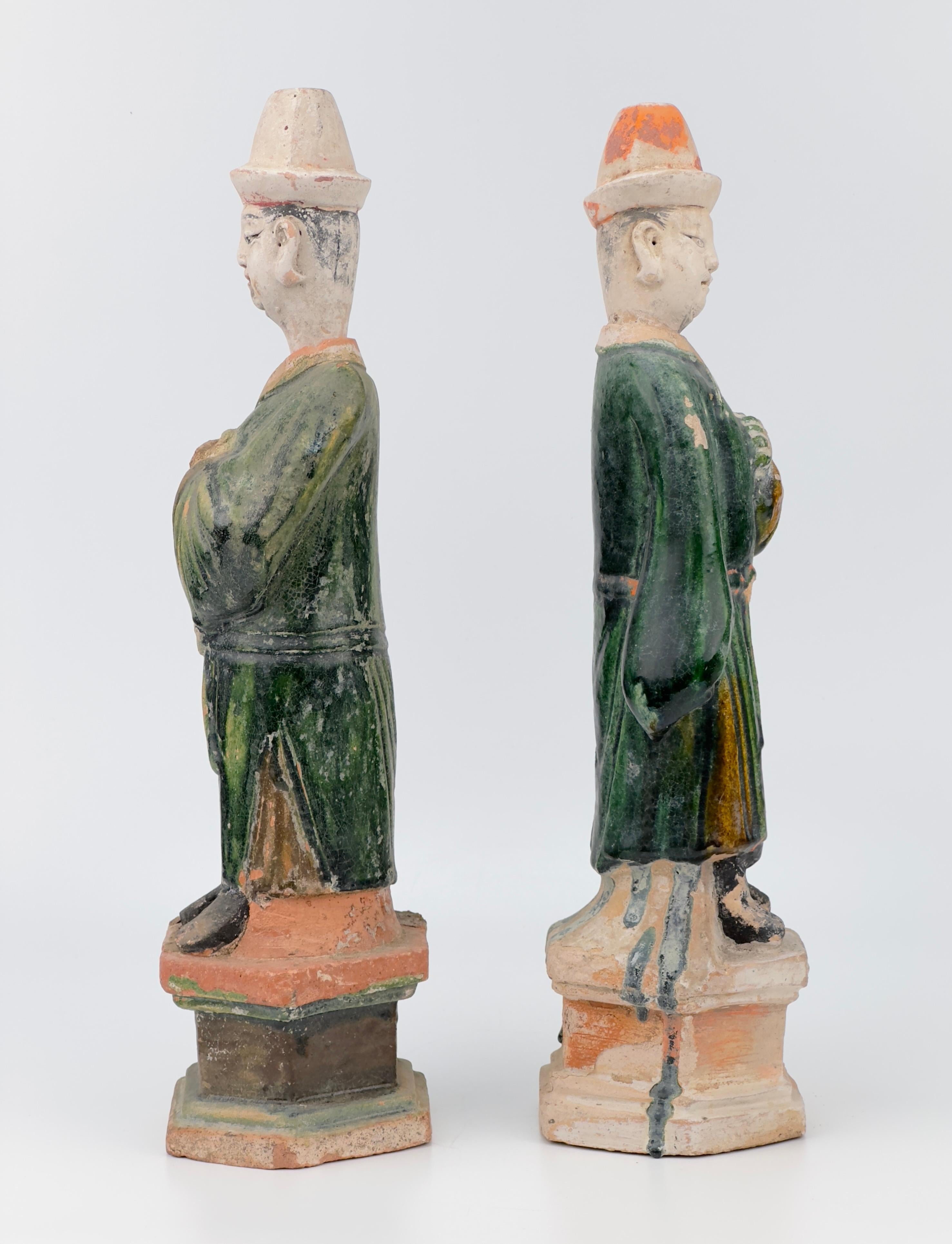 Statues of Chinese dignitaries crafted from terracotta, featuring glazes in green and ocher, are set on rectangular bases. The wide-sleeved robes and craftsmanship, along with the cylindrical flat hats with detachable head, indicate their Chinese