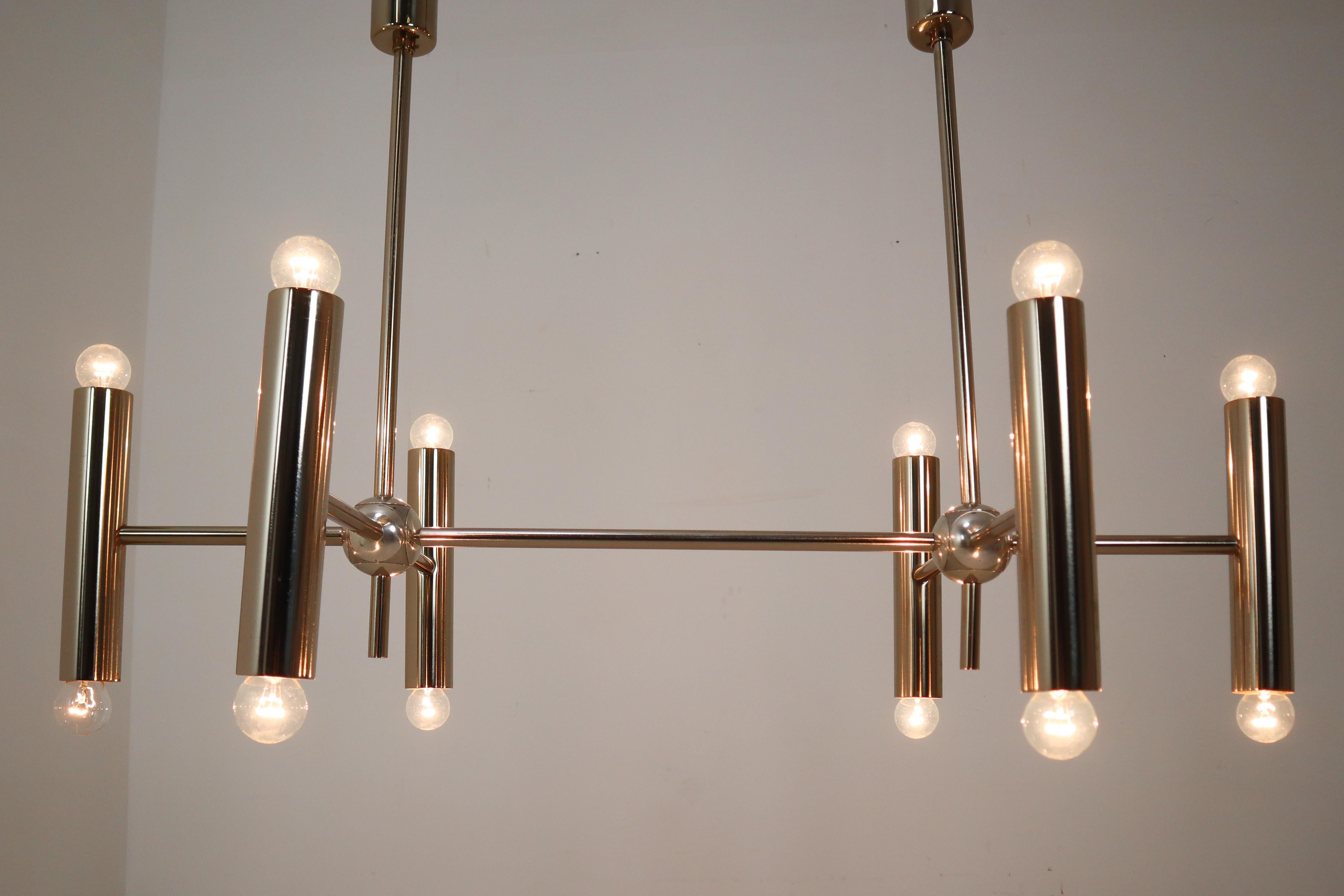 Mid-Century Modernist large chandelier with contains twelve lights, arranged in a symmetrical pattern on both side of the tube. The fixture is made of metal/steel with a chrome patina. Therefore an interesting color is visible on the metal. A warm
