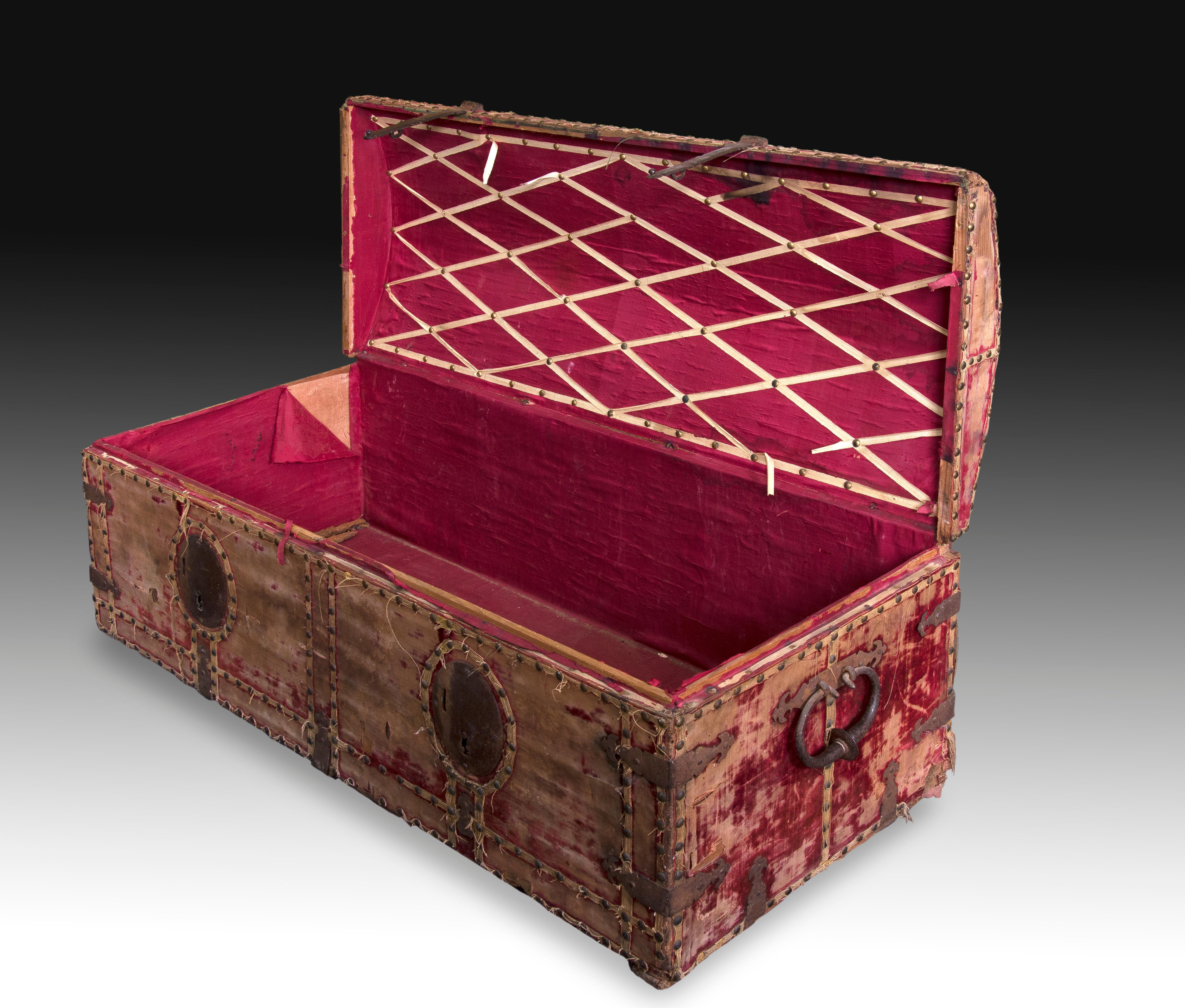 Rectangular chest with slightly curved lid that has two locks, handles and a series of ironwork and vintage studs in wrought iron, on the textile that covers it to the outside (also present inside the piece). These furniture for storing valuables