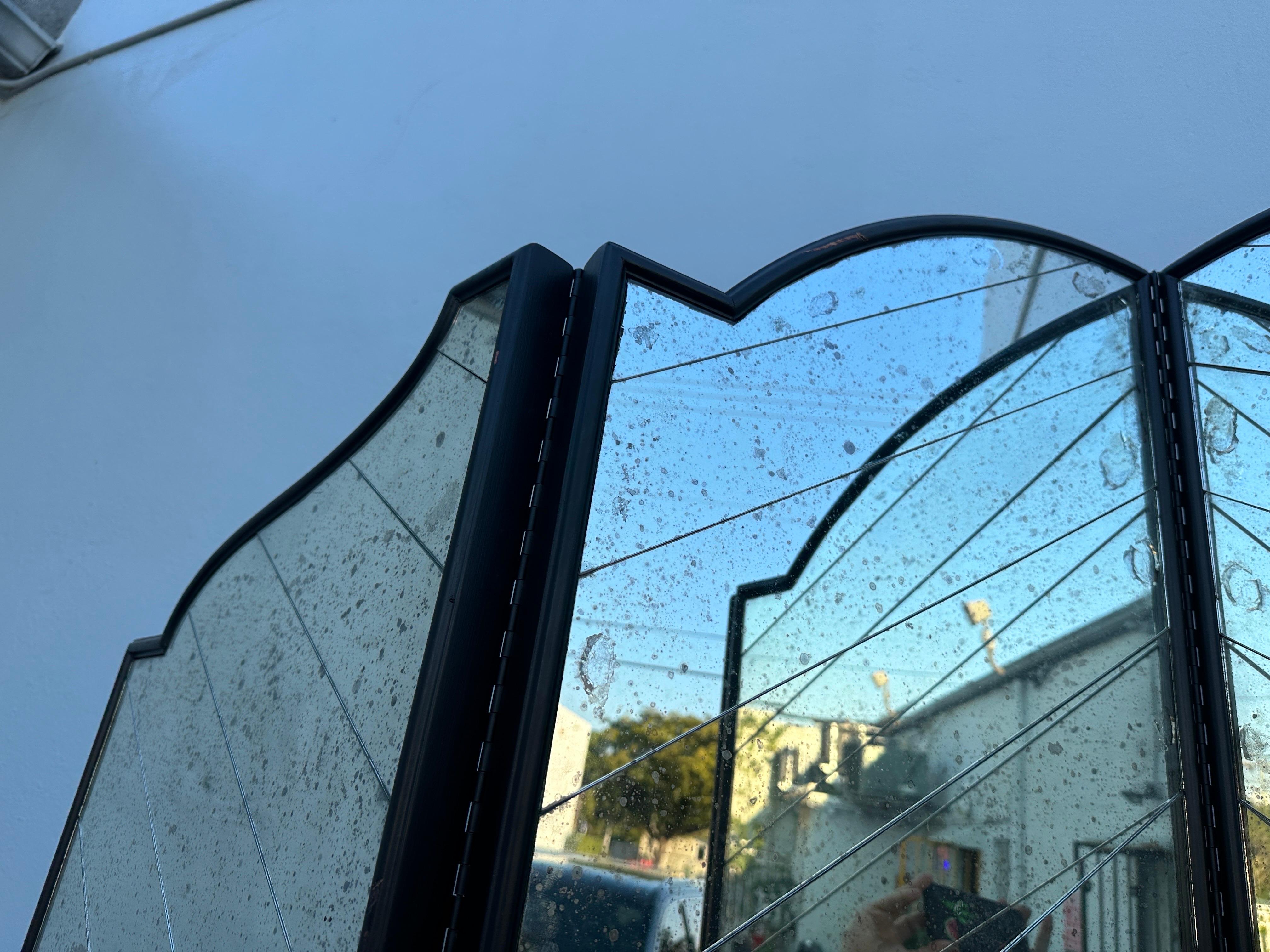 Questo paravento a 4 pannelli smerlati Hollywood Regency, perfettamente conservato, è disponibile in due versioni. Il vetro a specchio è tagliato a strisce e montato ad angolo per ottenere un effetto sorprendente. Incorniciati in legno nero e