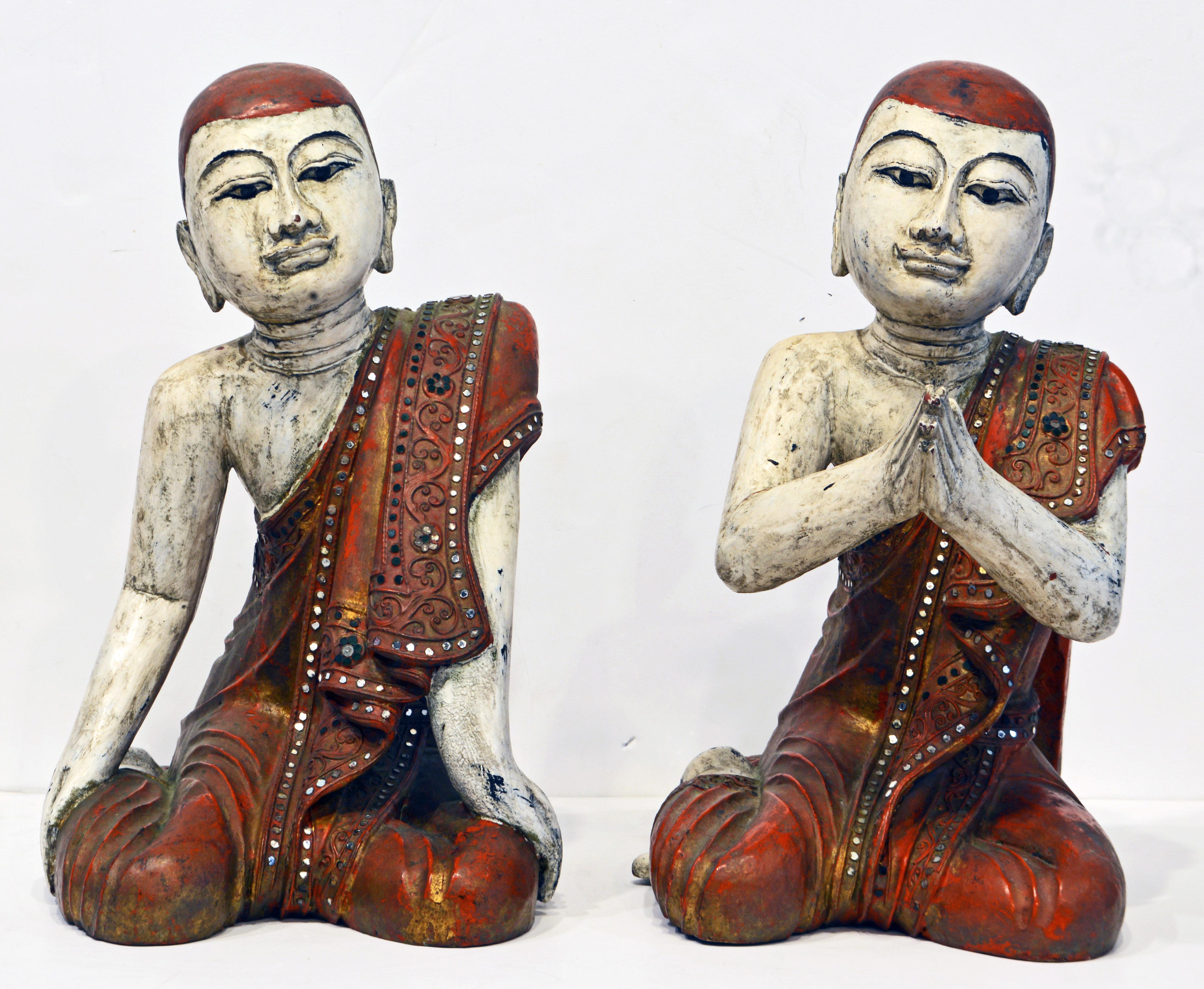 16 inches tall these two Thai or Burmese young monks are carved in wood and painted One monk is sitting in a praying position, the other with a relaxed but still devoted posture. They wear beautifully glass bejeweled red robes with inlay and